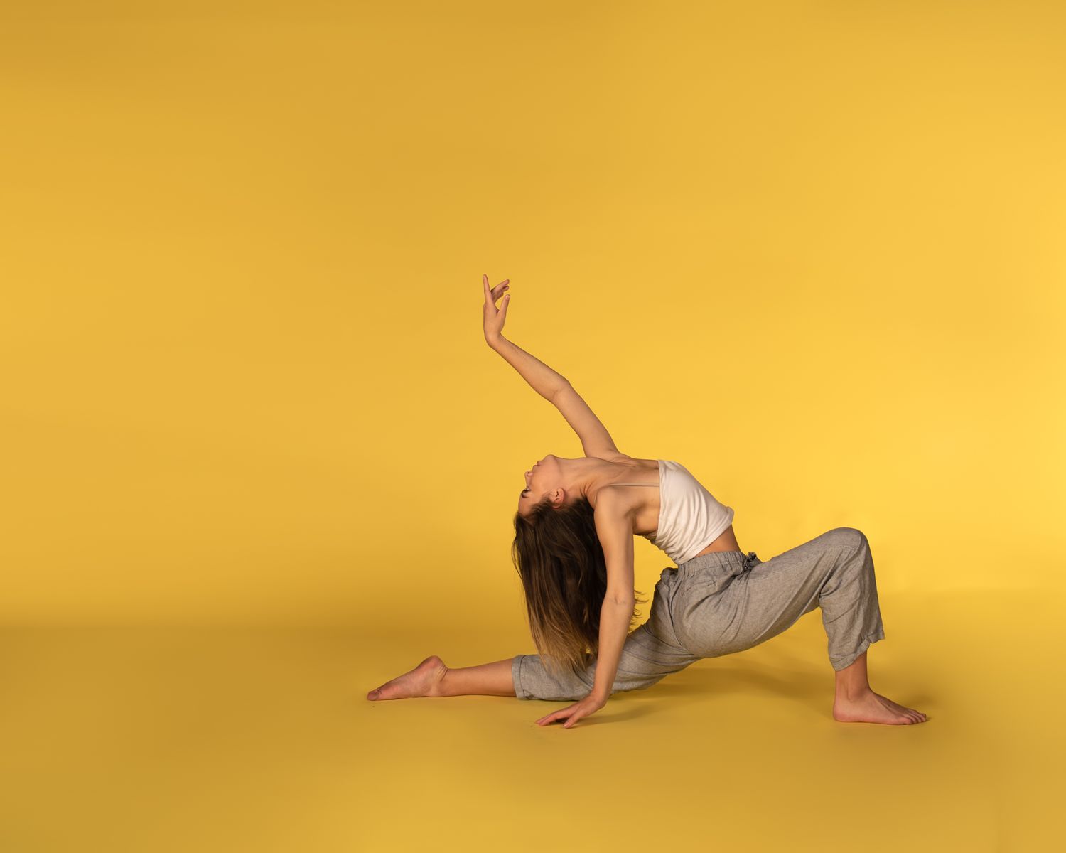 Elegant dancer in flowing gray outfit performs contemporary dance move against vibrant yellow backdrop.