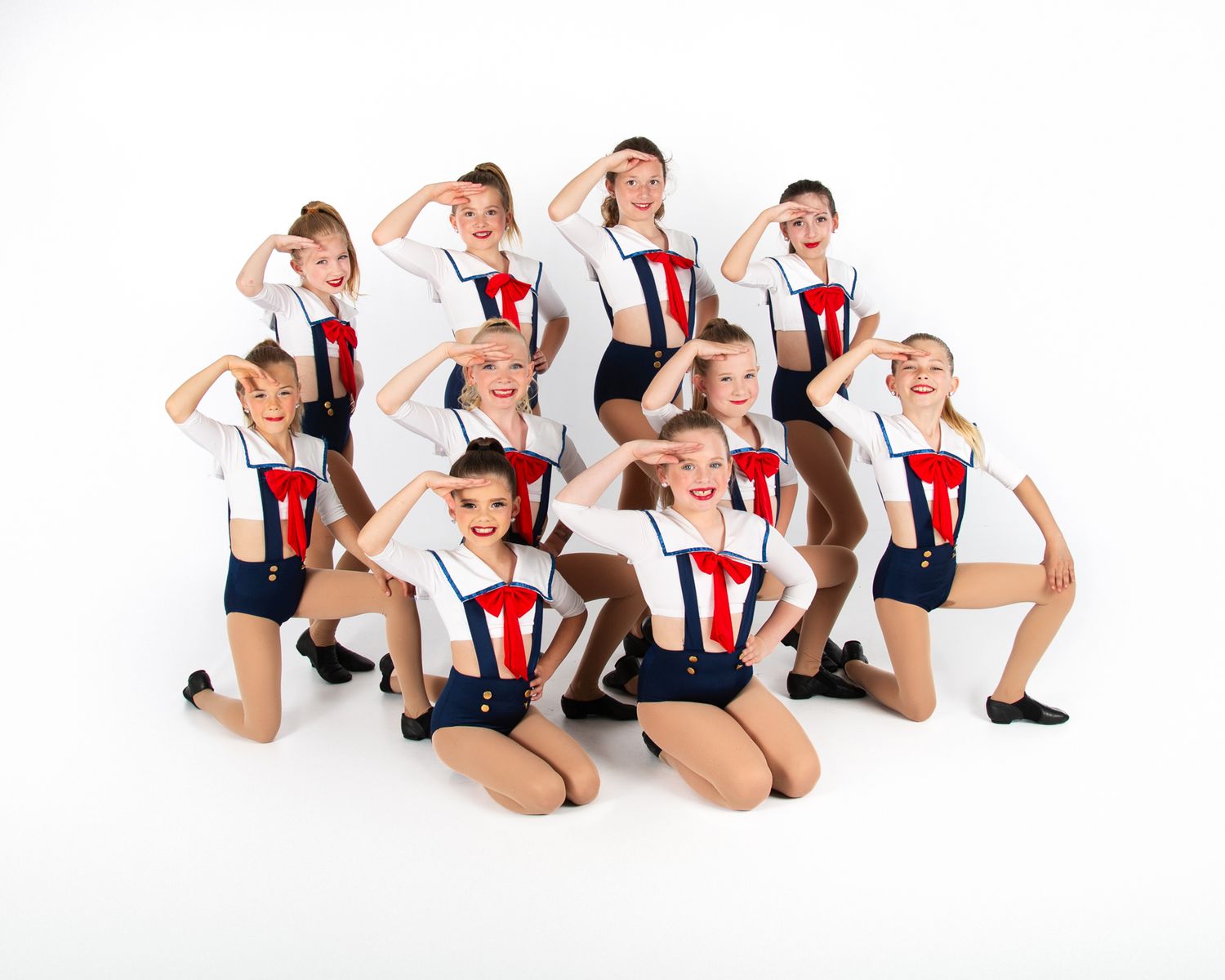 Dance group in matching sailor-inspired costumes striking synchronized pose on white background.
