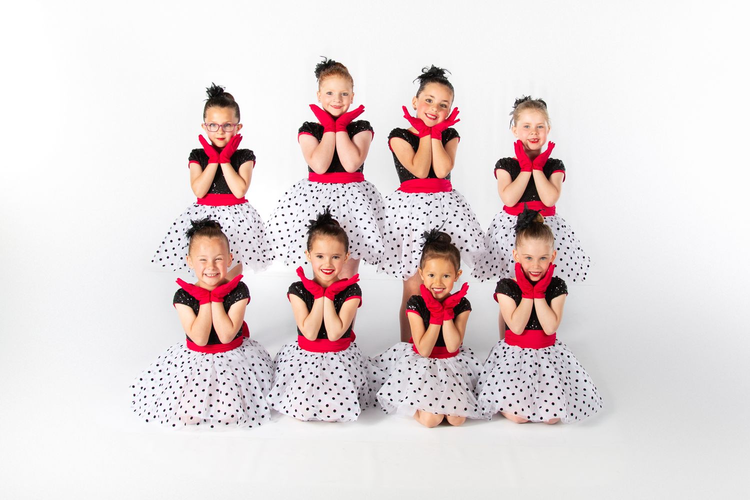 Young dancers in polka dot dresses and red necklines pose together in a studio setting.