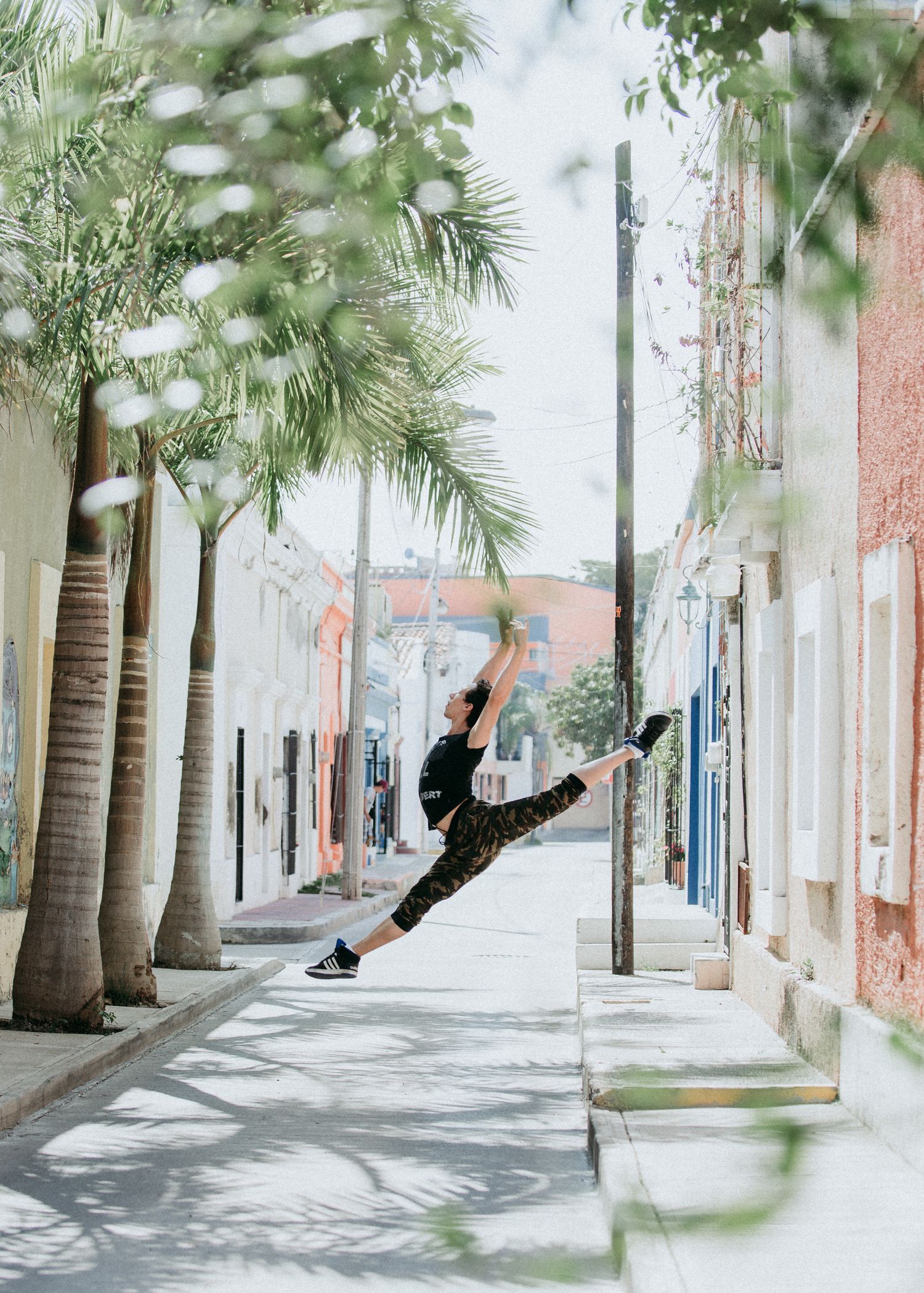 Dancer performs a dramatic split leap on a palm tree-lined street in Old San Juan, with colonial architecture in view.
