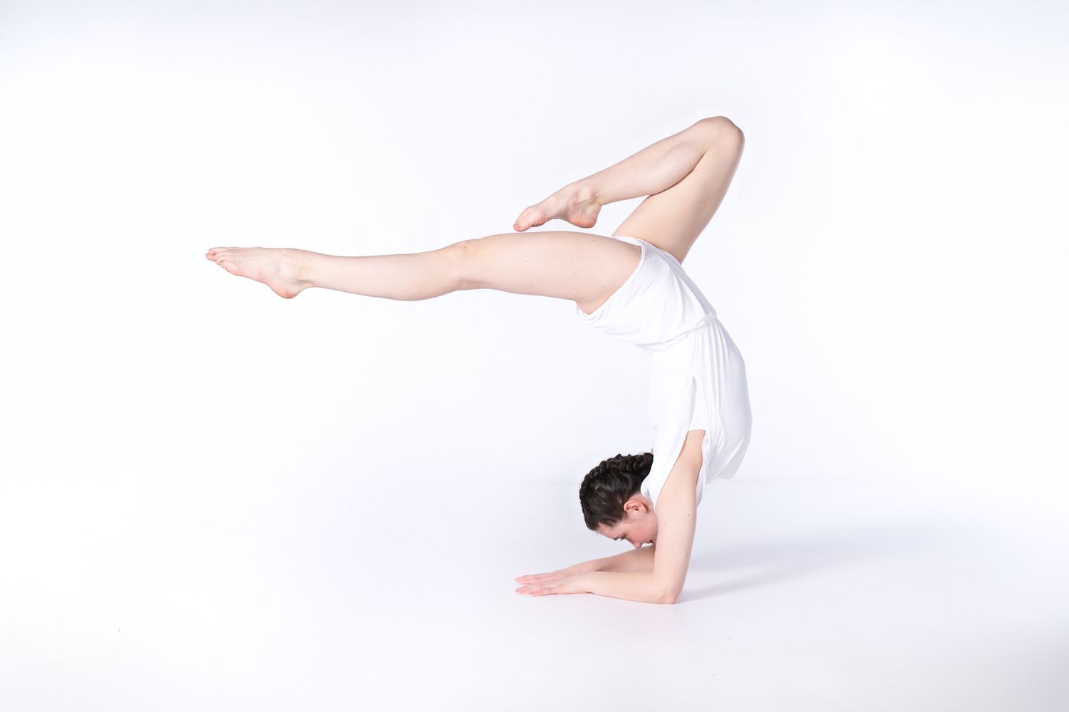 Gymnast in white leotard performs advanced handstand with split legs.