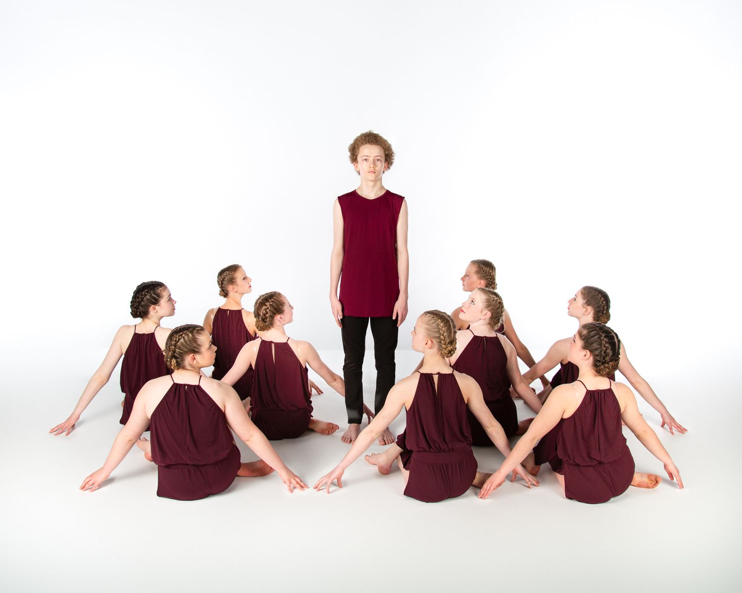 Contemporary dance group in burgundy costumes creating artistic formation on white background.
