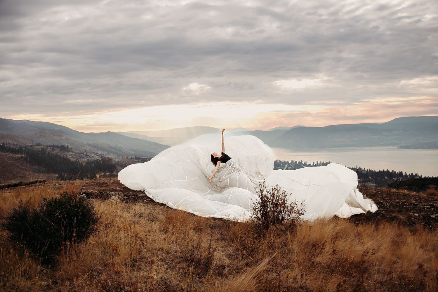 Aerial shot of a lone skydiver descending near a snow-covered mountain peak against a moody cloudy sky.