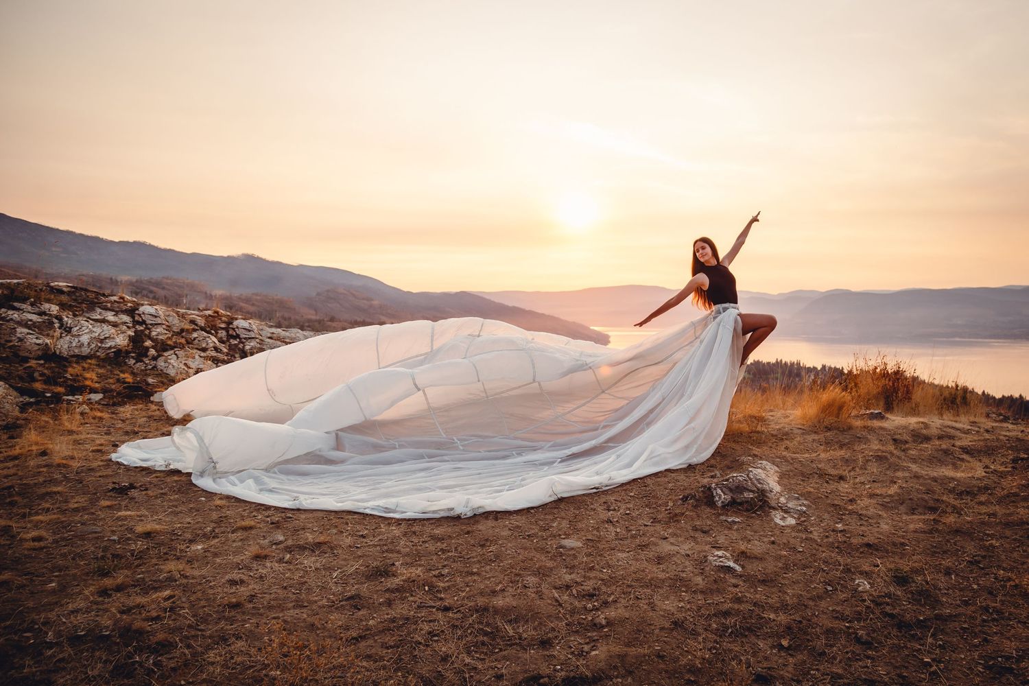A flowing white wedding dress billows dramatically against a golden mountain sunset backdrop.