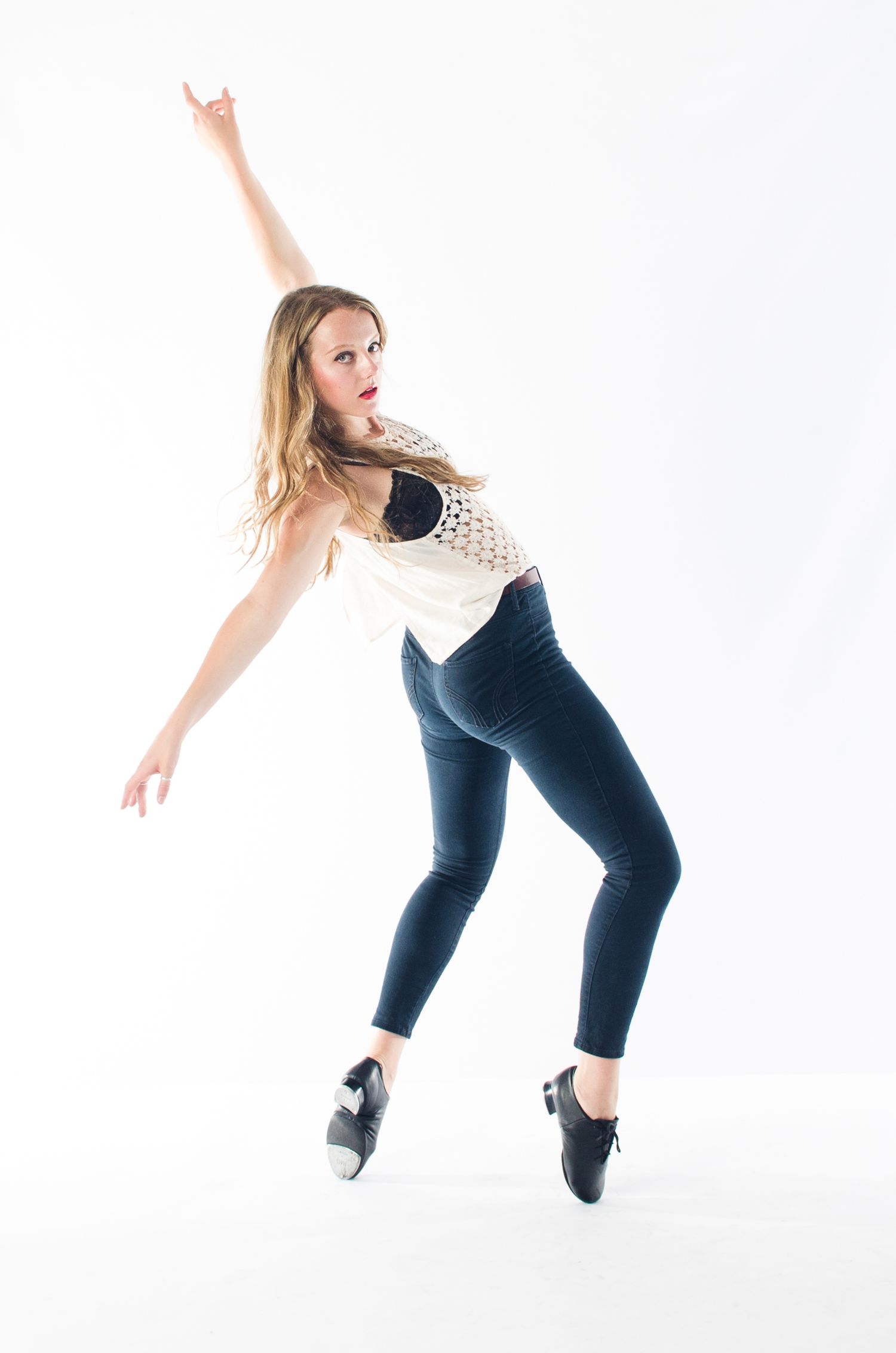 Dancer in casual wear strikes graceful pose while jumping in studio with white background.
