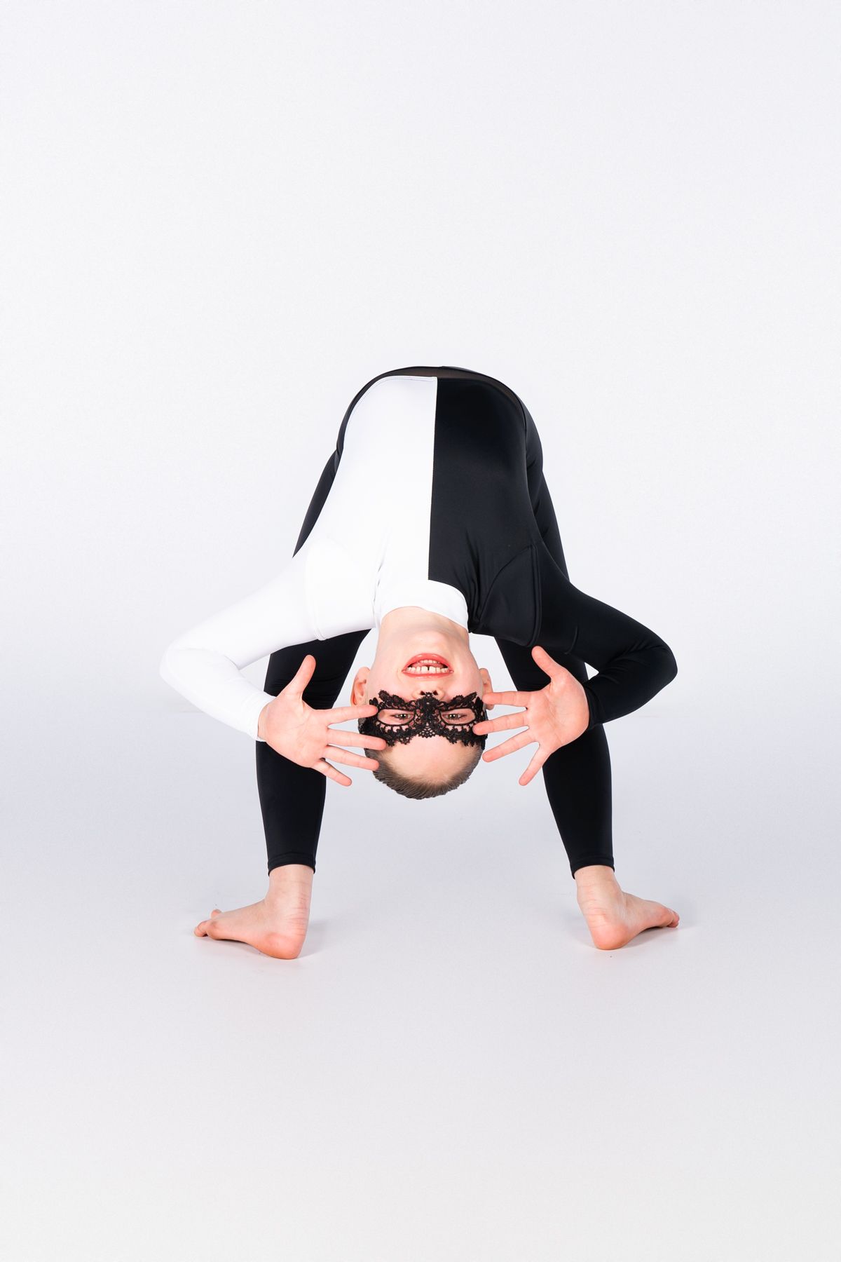 A dancer in black attire performs a forward bend pose on a white background.