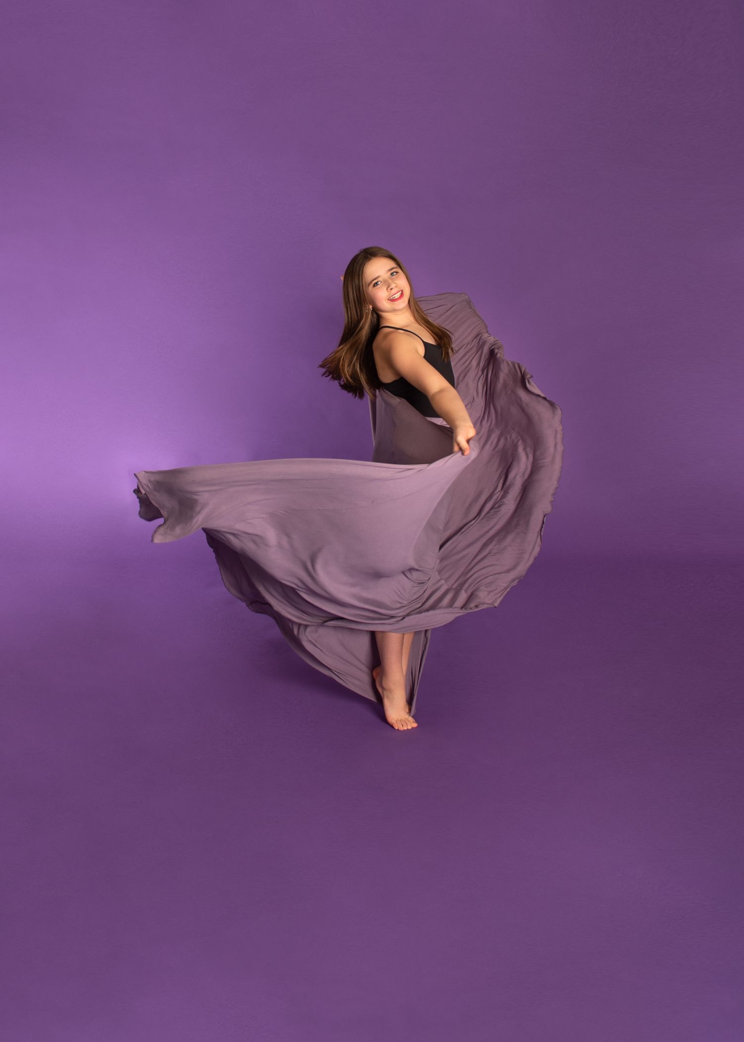 A person dances gracefully in a flowing lilac dress against a purple background, creating an elegant swirling motion.