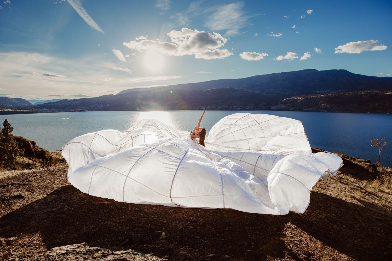 A white mattress sits on a cliff overlooking a scenic lake and mountains on a sunny day.