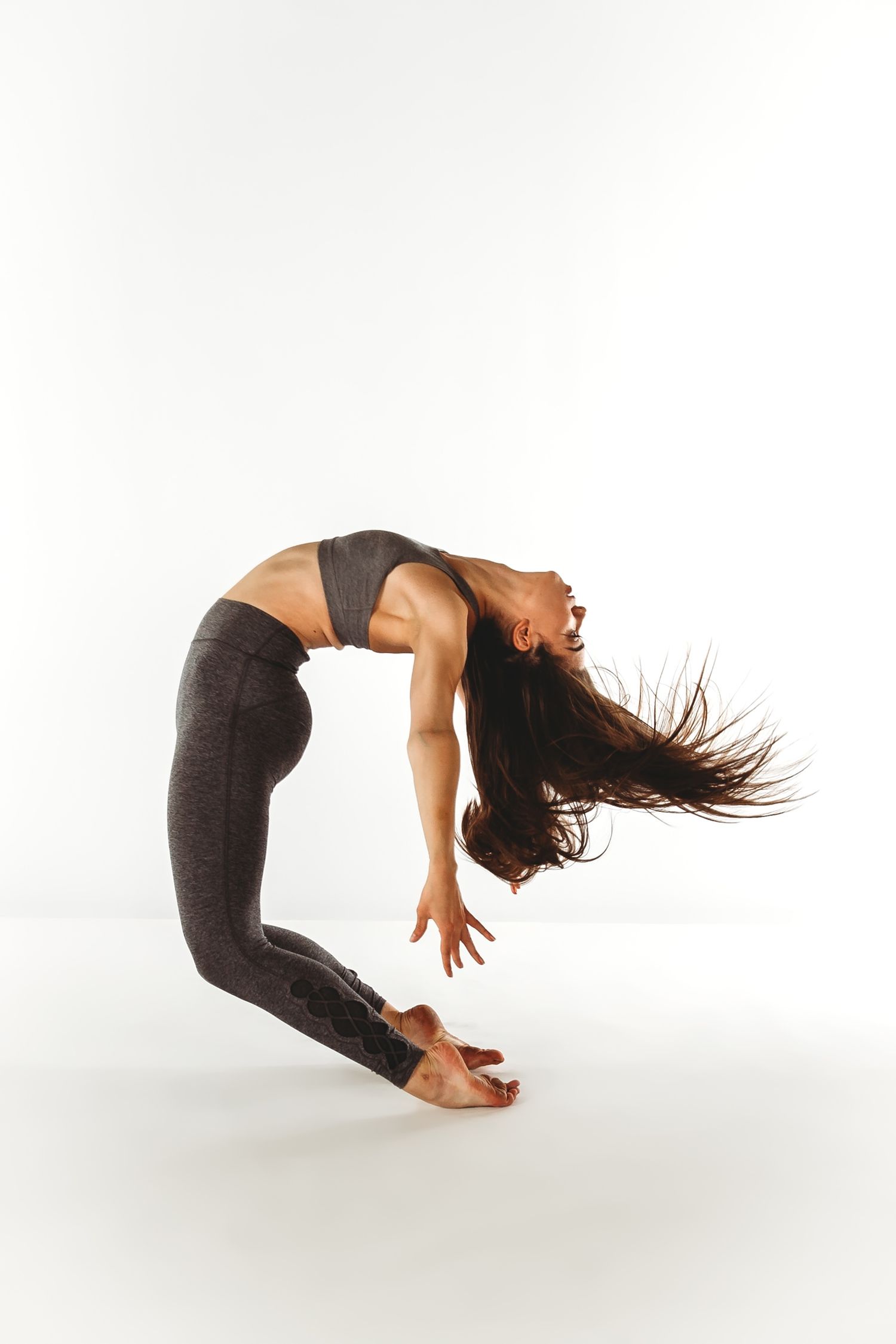 Dancer in athletic wear performs dramatic backbend with flowing hair against white background.