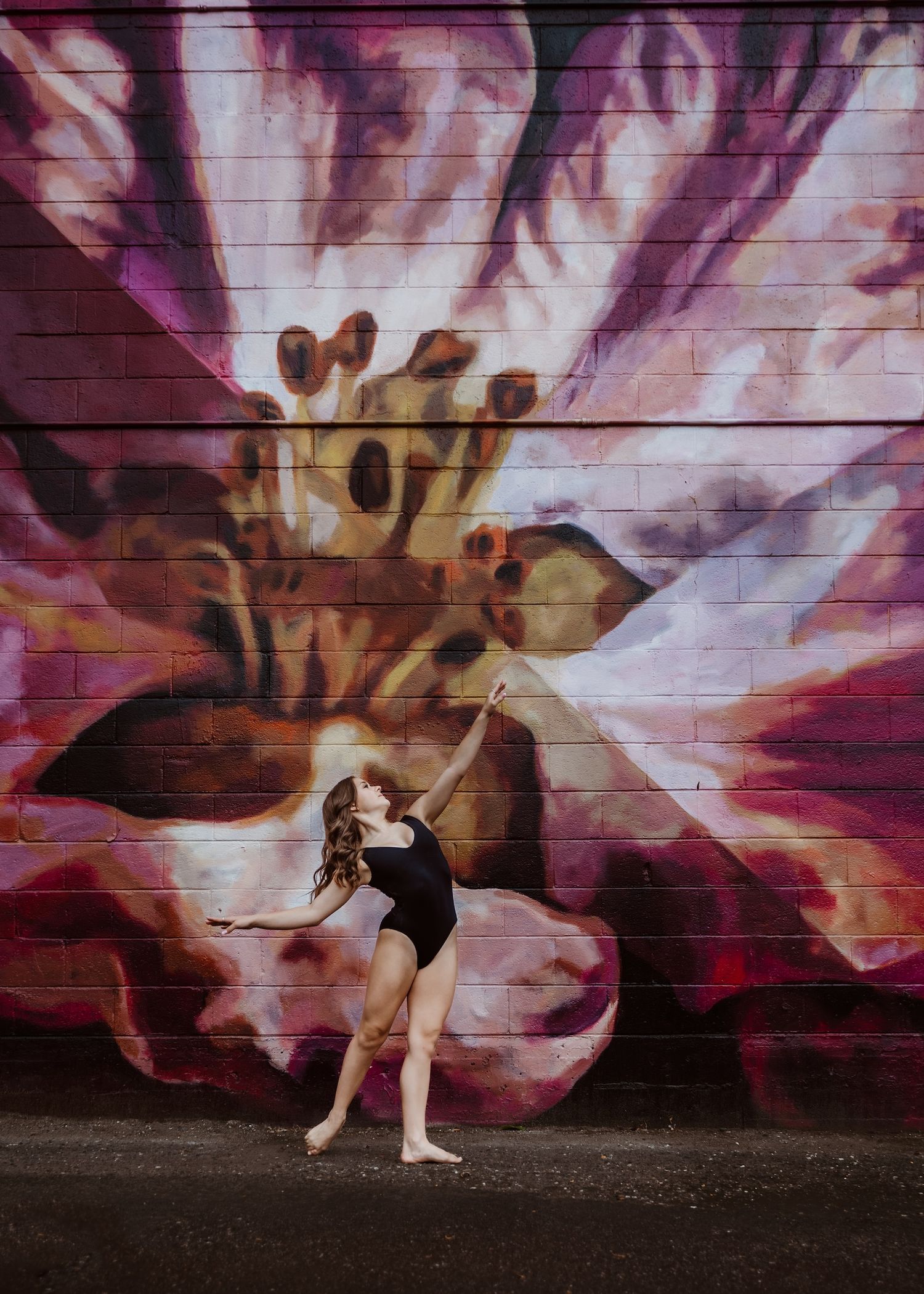 Dancer strikes elegant pose against vibrant purple floral mural on urban wall.
