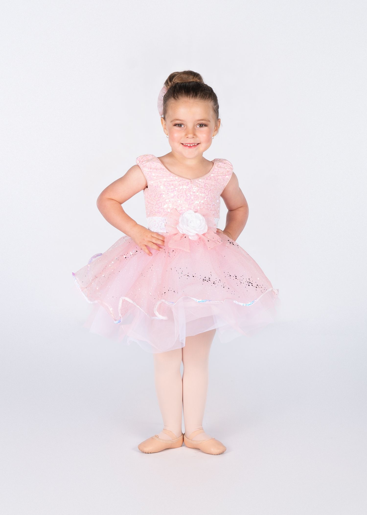 Young dancer in pink tulle dress and ballet position stands against white background.