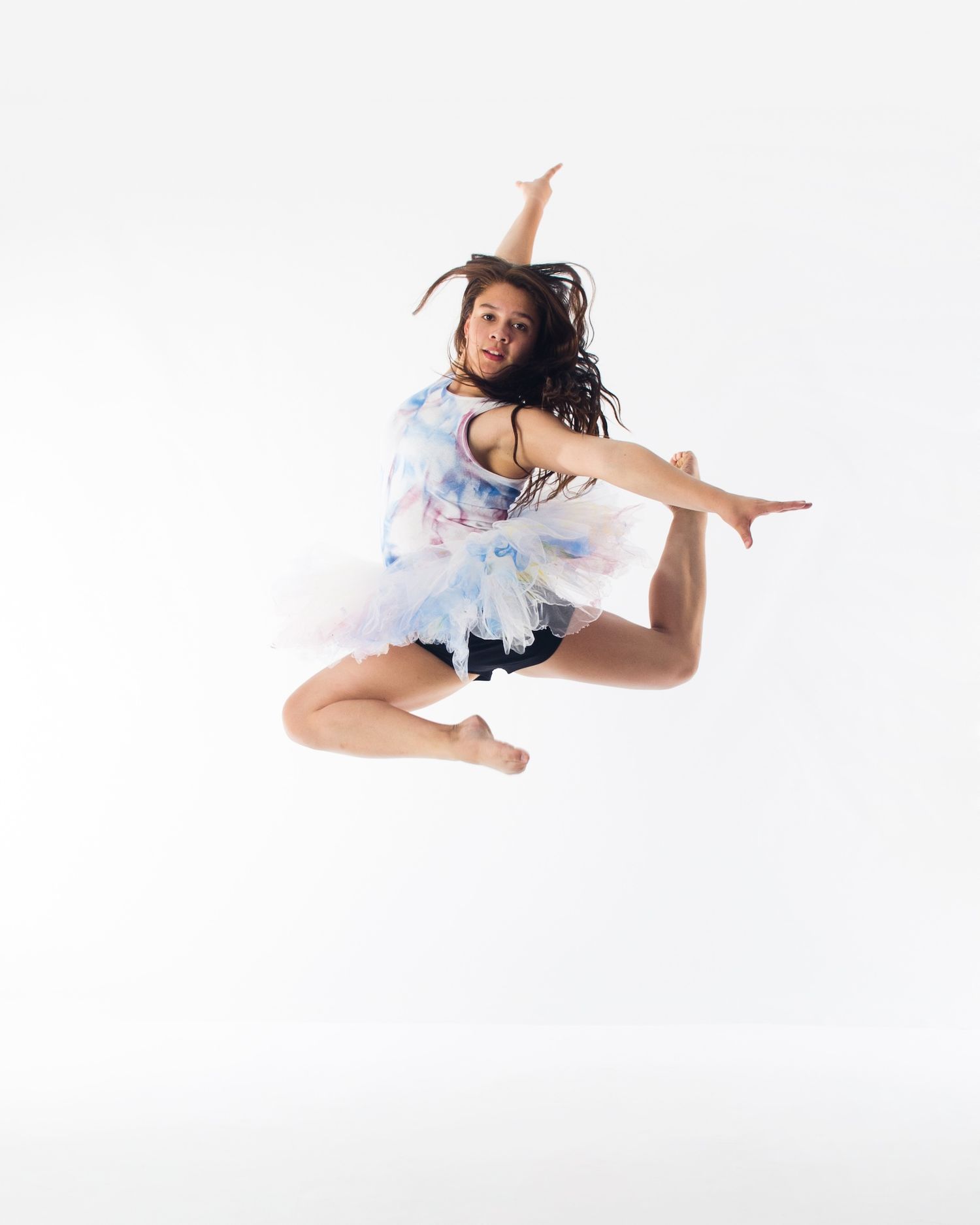 Dancer in a light blue costume performs a graceful leap against a white background during a contemporary dance routine.
