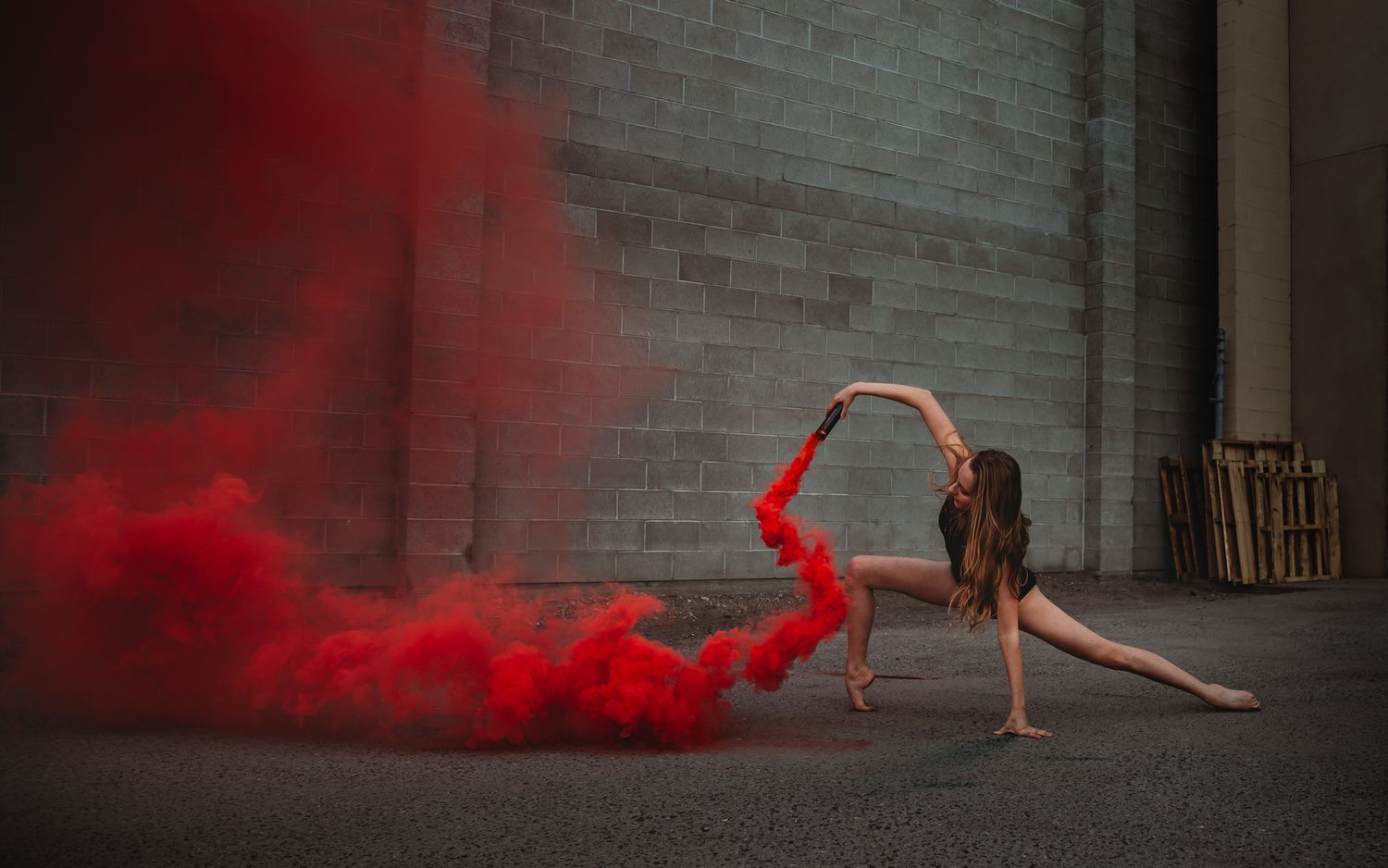 A dancer performs in an industrial setting with dramatic red smoke trails creating an artistic flowing effect.