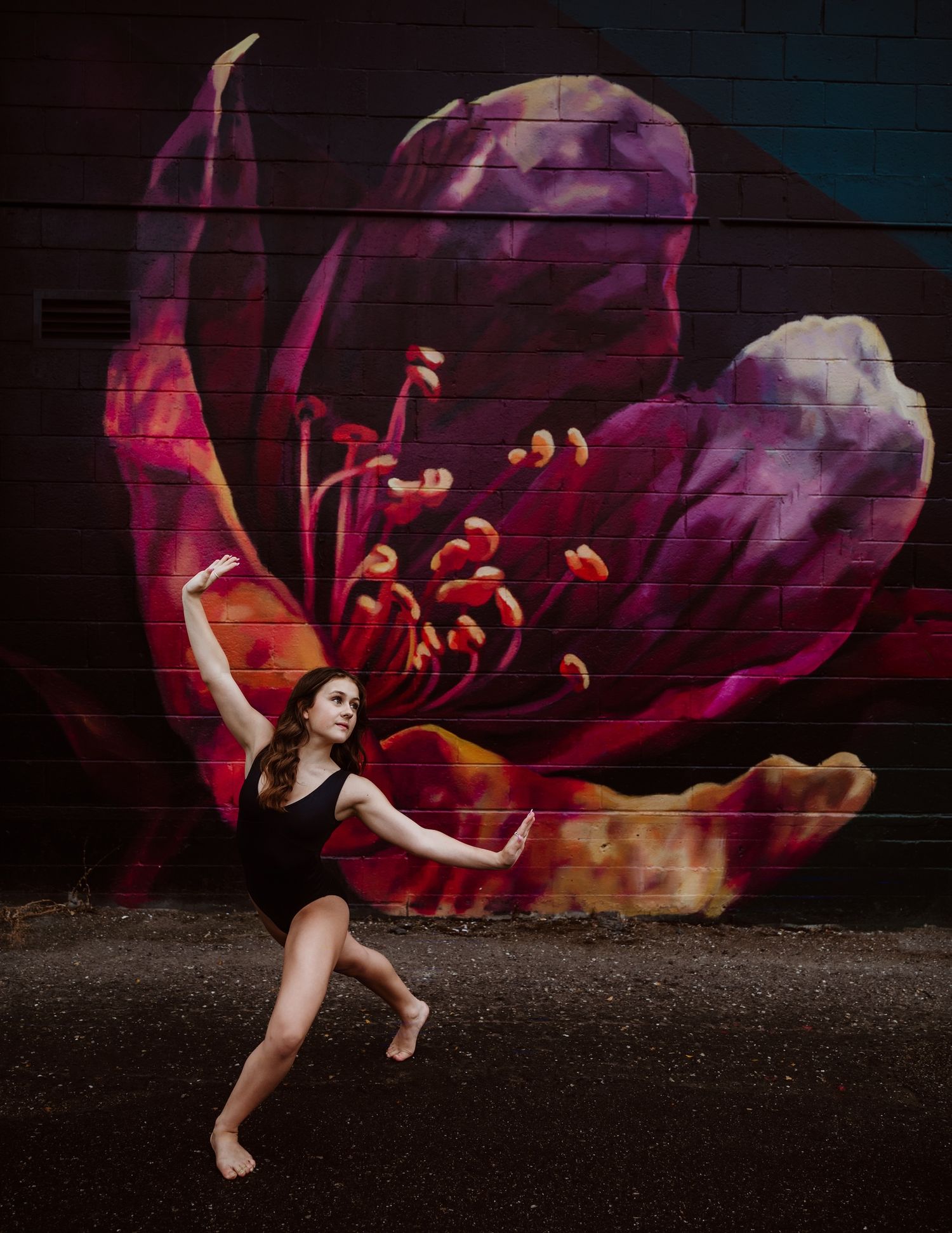 Artistic dance pose performed in front of dramatic dark purple flower mural on brick wall.