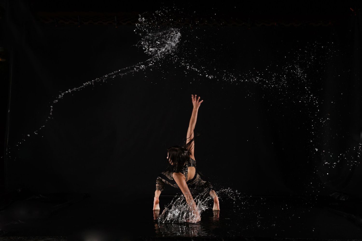 A person emerges from dark water splashing upward with a dramatic spray of droplets against a black background.