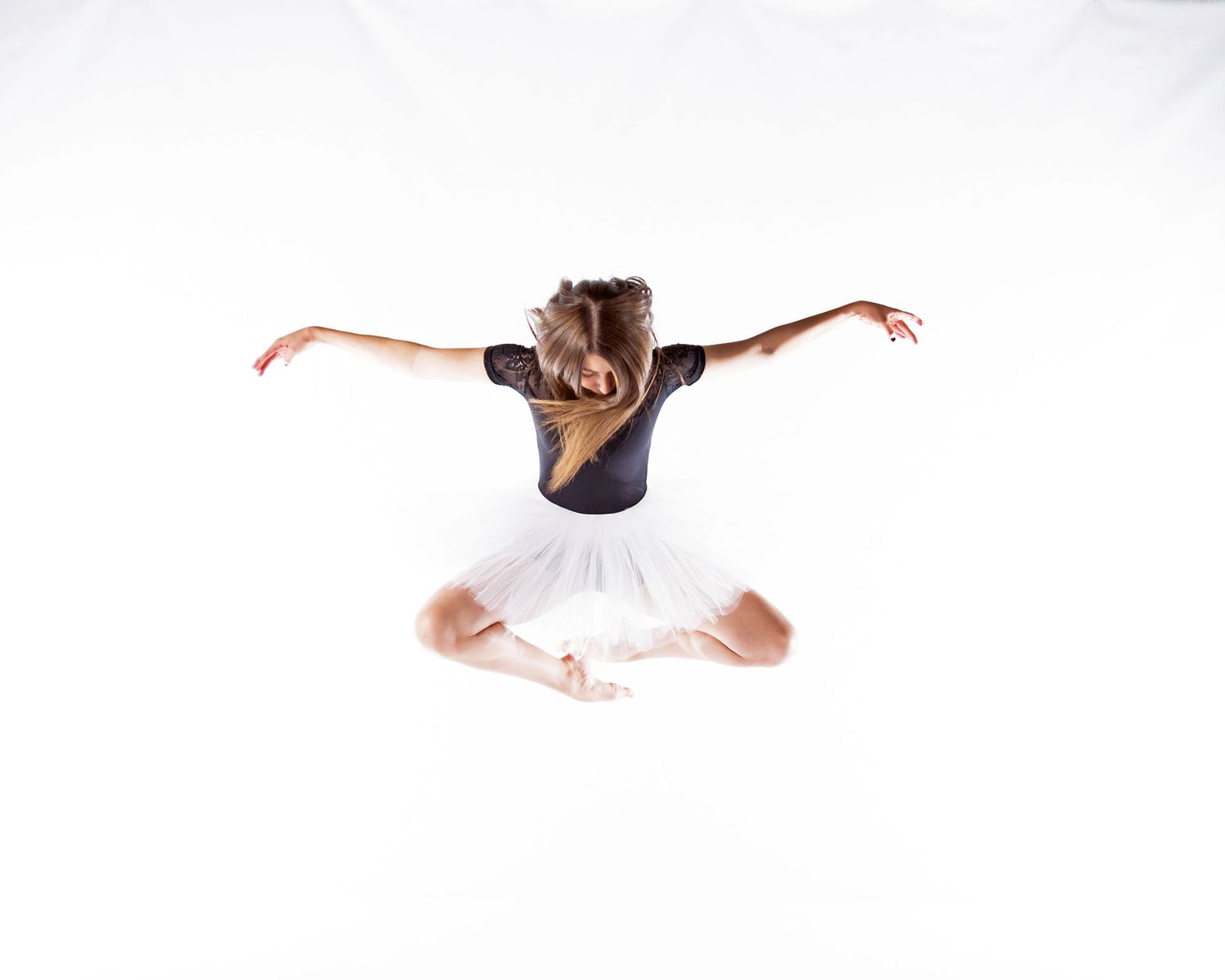 Dancer in black top and white tutu executing graceful jump with outstretched arms.
