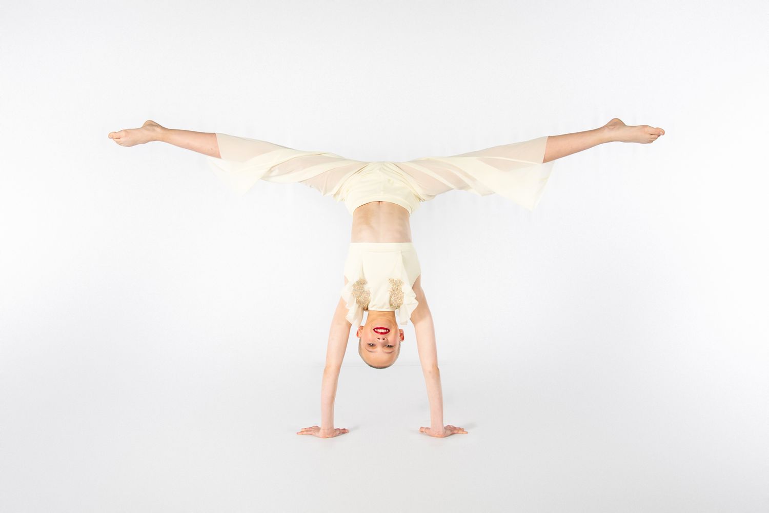 A person performing a handstand against a white background showing strength and balance in a minimalist setting.