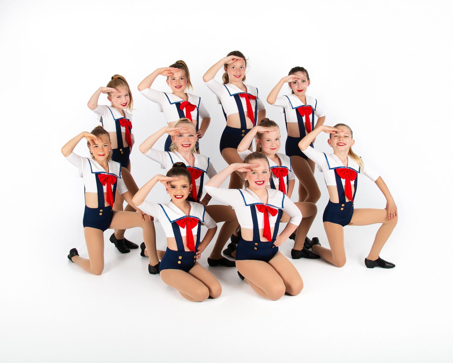 Dance group in matching sailor-inspired costumes poses together in formation on white background.