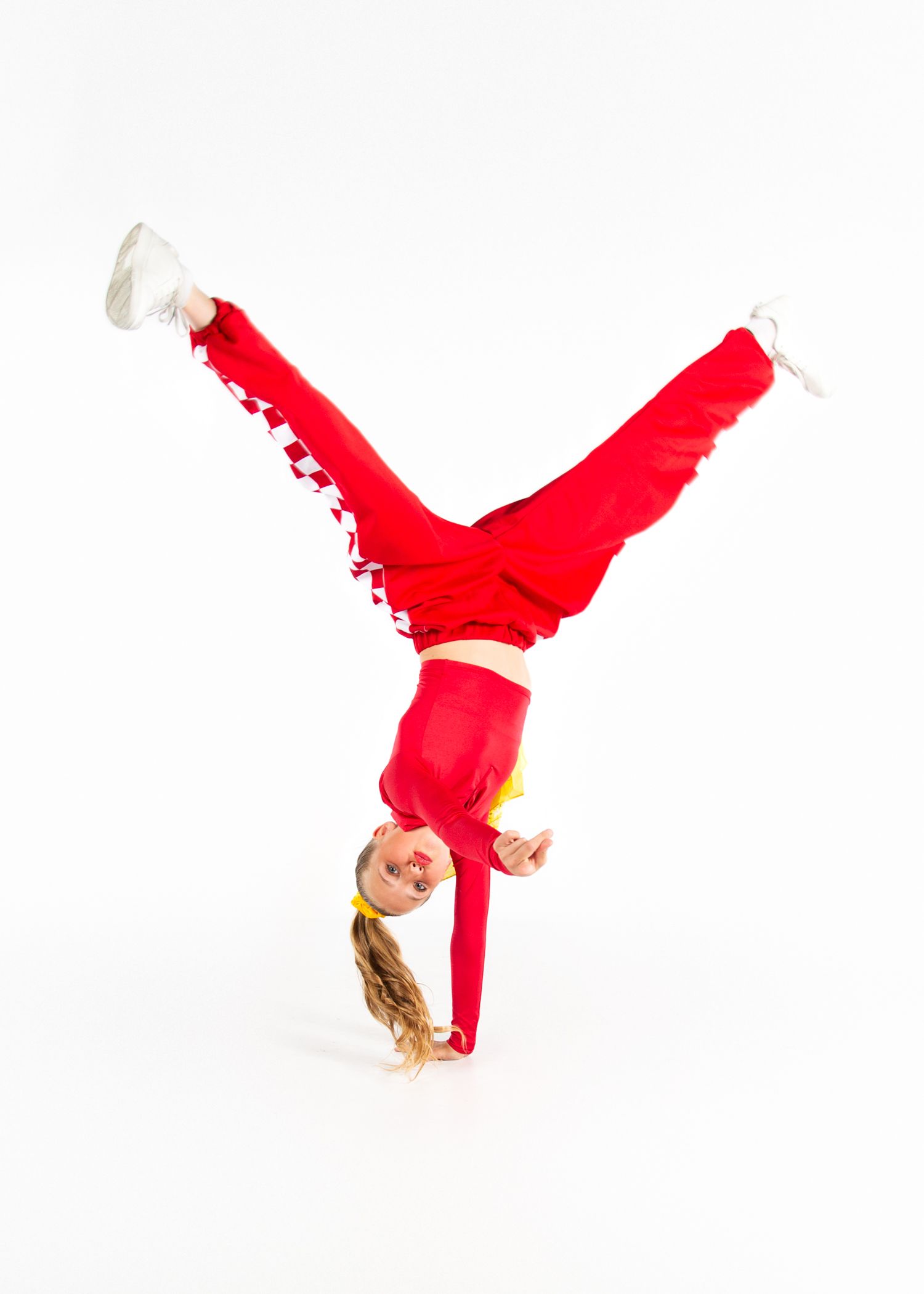 A gymnast in a bright red outfit performs a handstand against a white background.