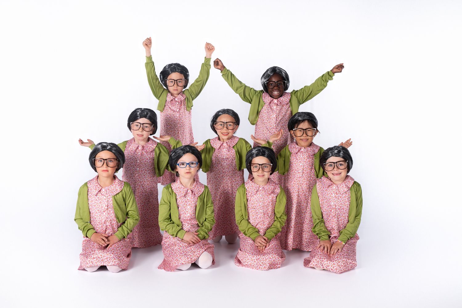 Group of dancers in matching pink and green costumes perform synchronized pose on stage.