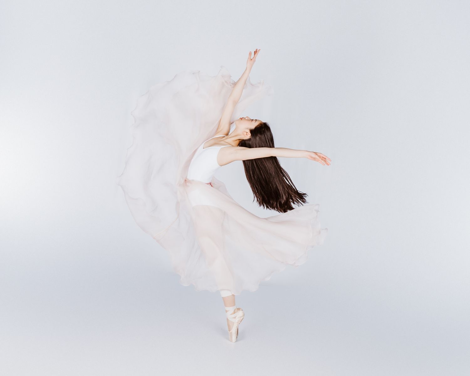 Graceful dancer in white dress creating elegant circular motion against light background.