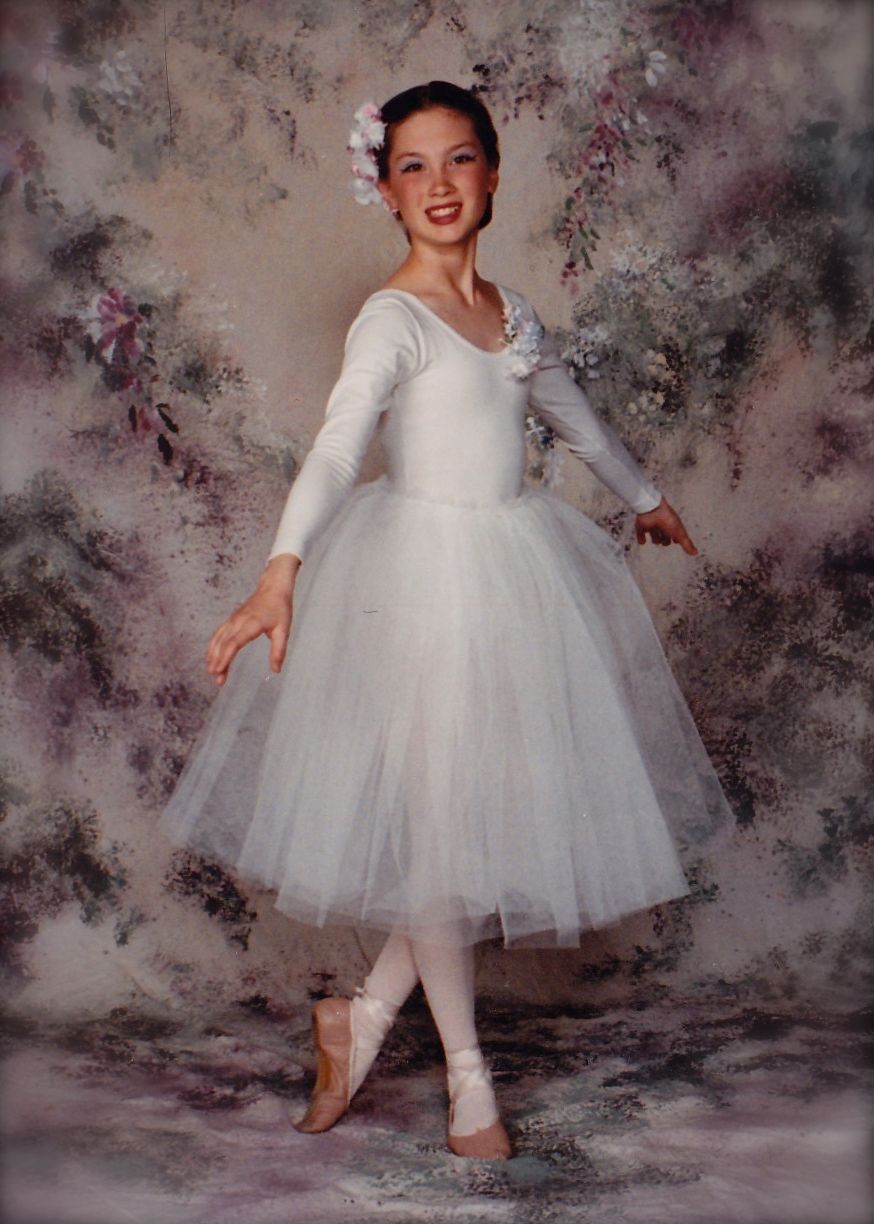 Ballet dancer in white romantic tutu and pointe shoes poses gracefully against artistic backdrop.