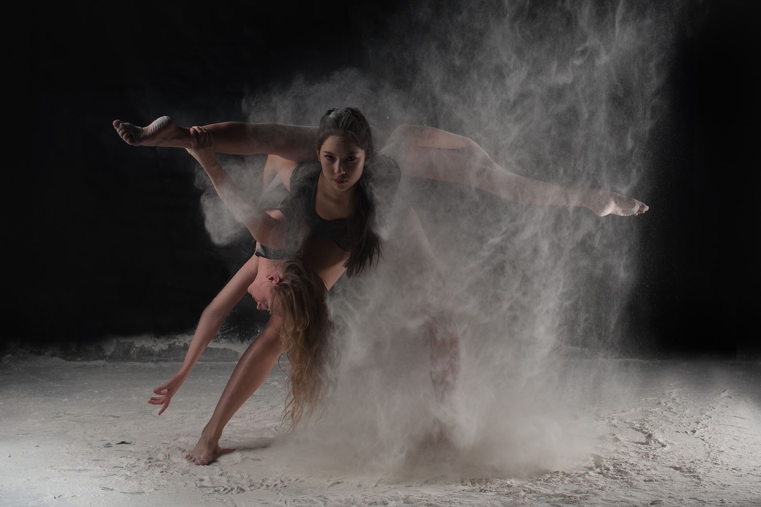 Dancer performs dramatic contemporary movement in cloud of white powder against dark background.