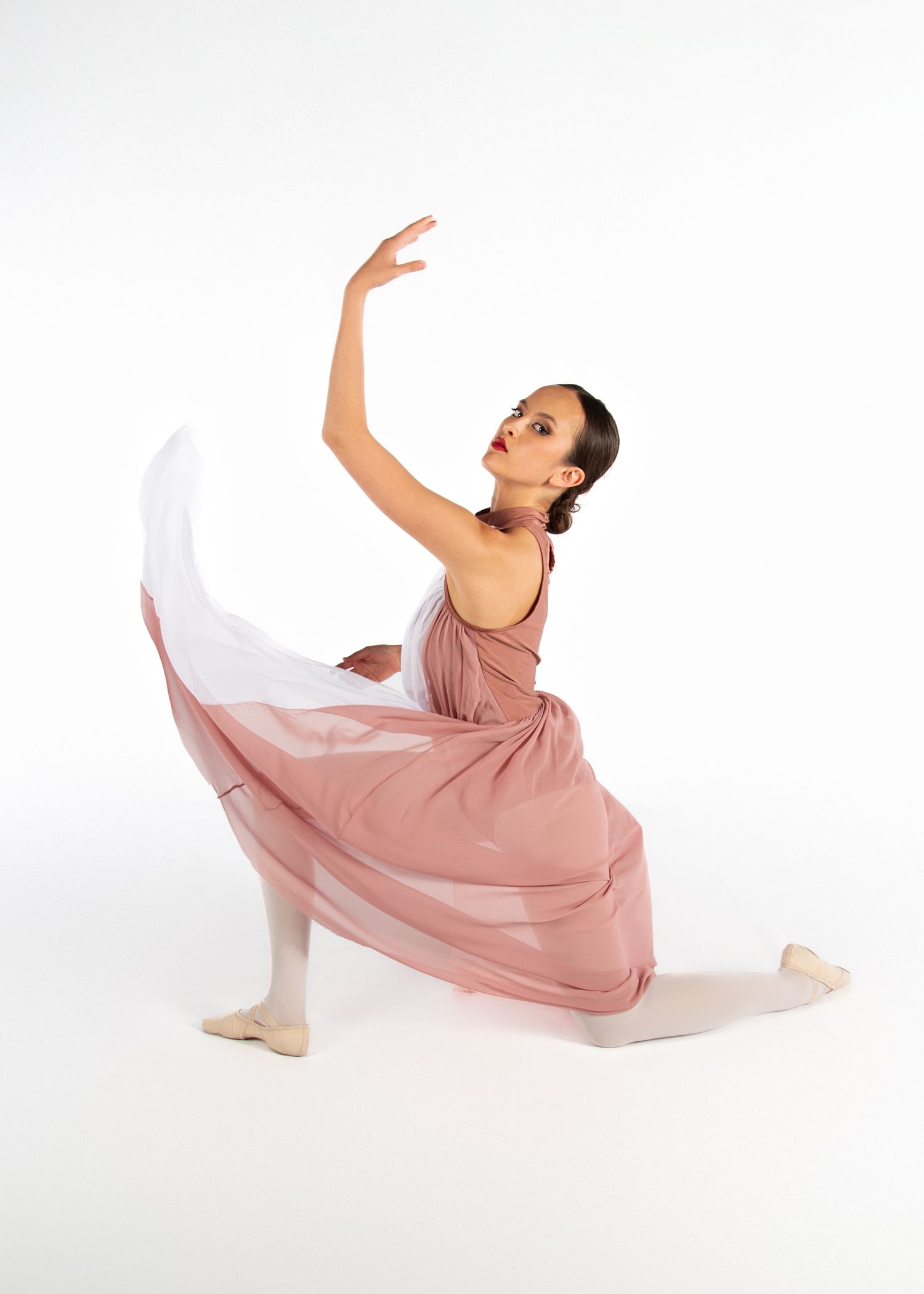 Ballet dancer in flowing dusty pink dress performing elegant pose with graceful arm movement.