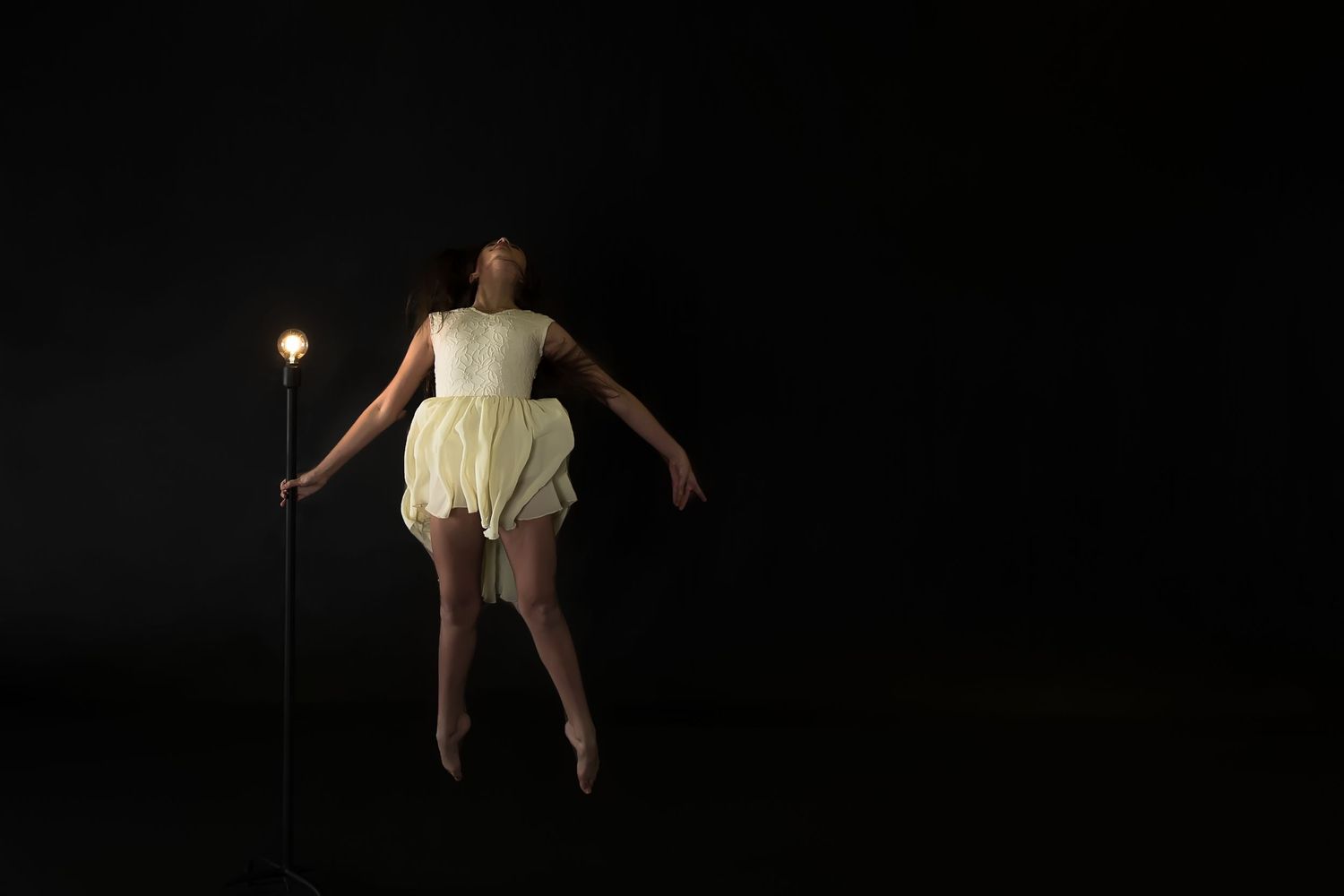 Figure in white dress illuminated against dark background floats while holding glowing wand in dramatic performance scene.