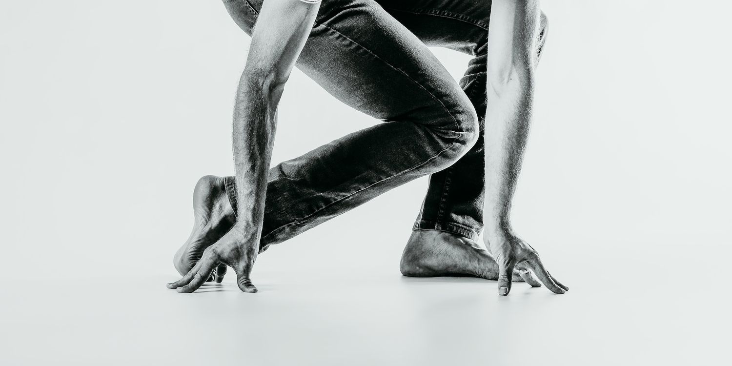 Athletic performer in starting position with hands on ground and legs bent in dramatic black and white.