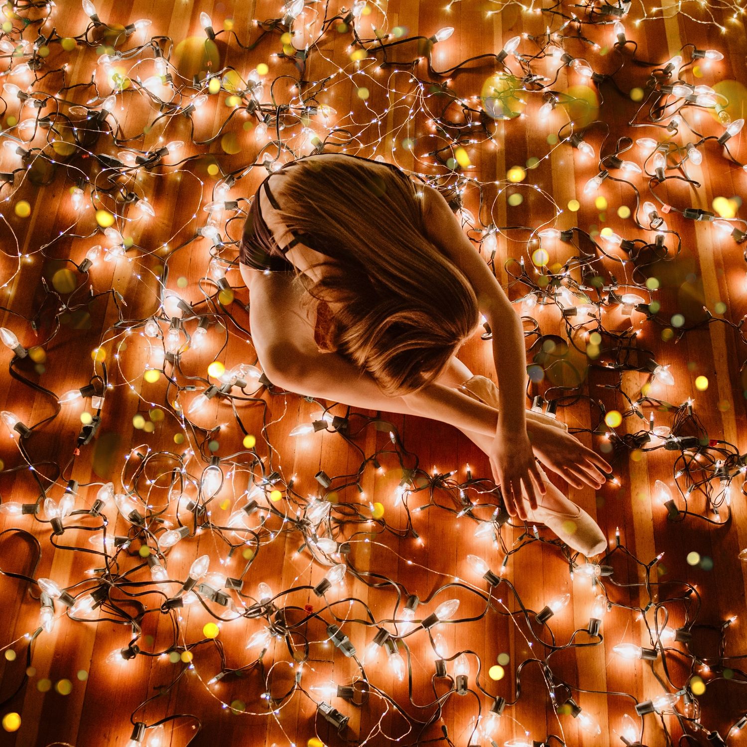 Graceful figure bathed in warm glow of hanging string lights creating magical ambient effect.