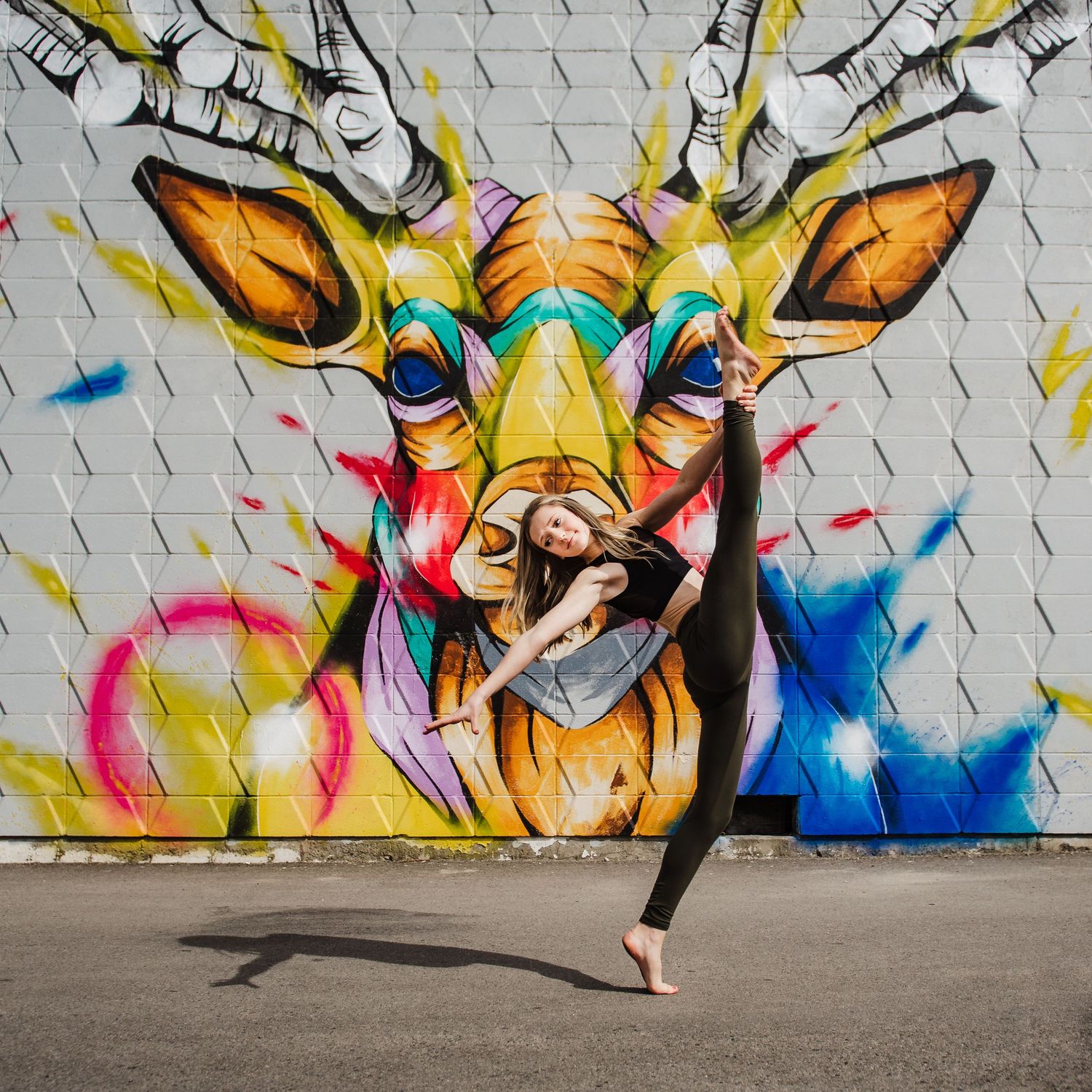 Dancer performs elegant pose against vibrant graffiti wall featuring colorful giraffe street art mural.