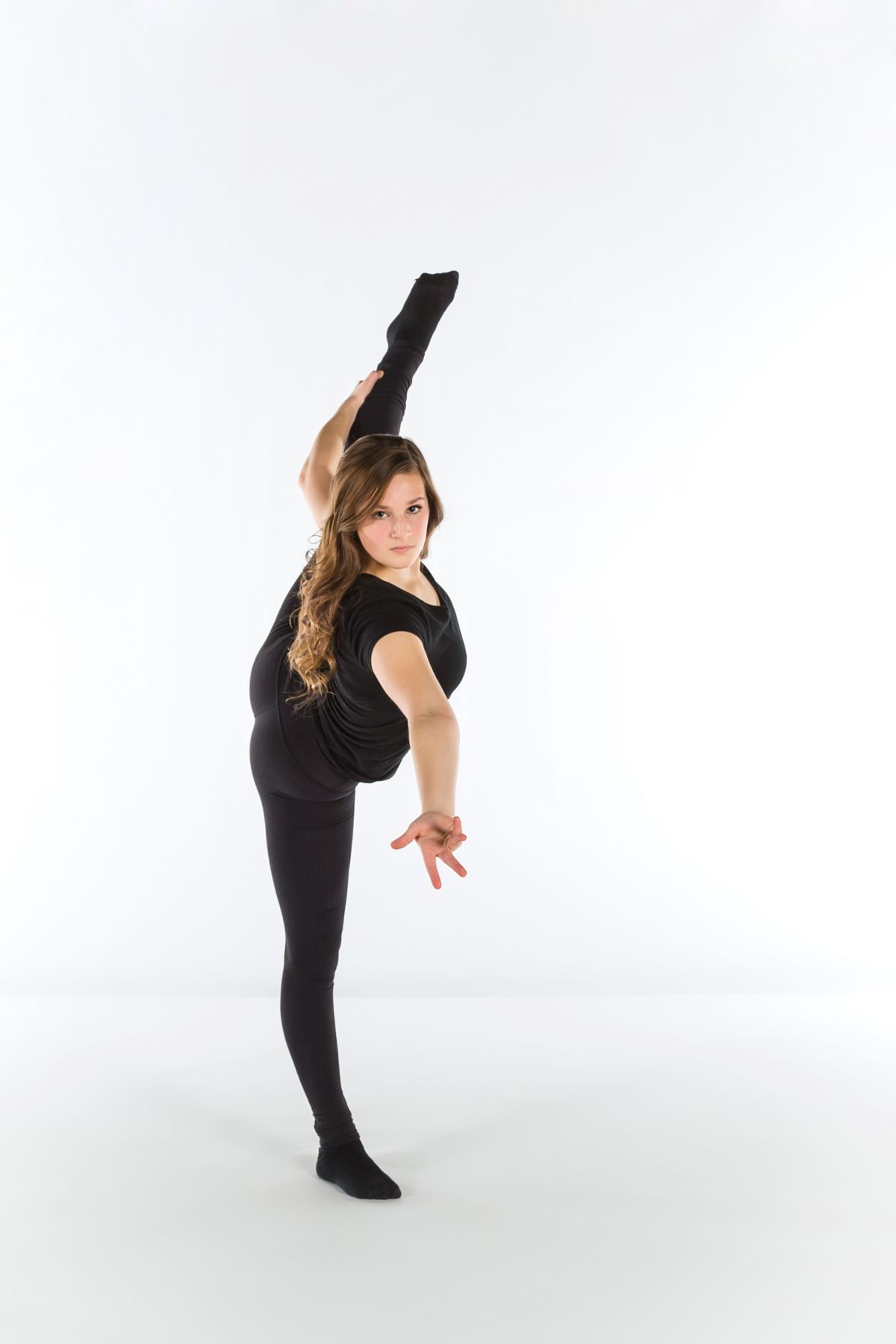 A dancer in black attire performs a standing split pose against a white backdrop.