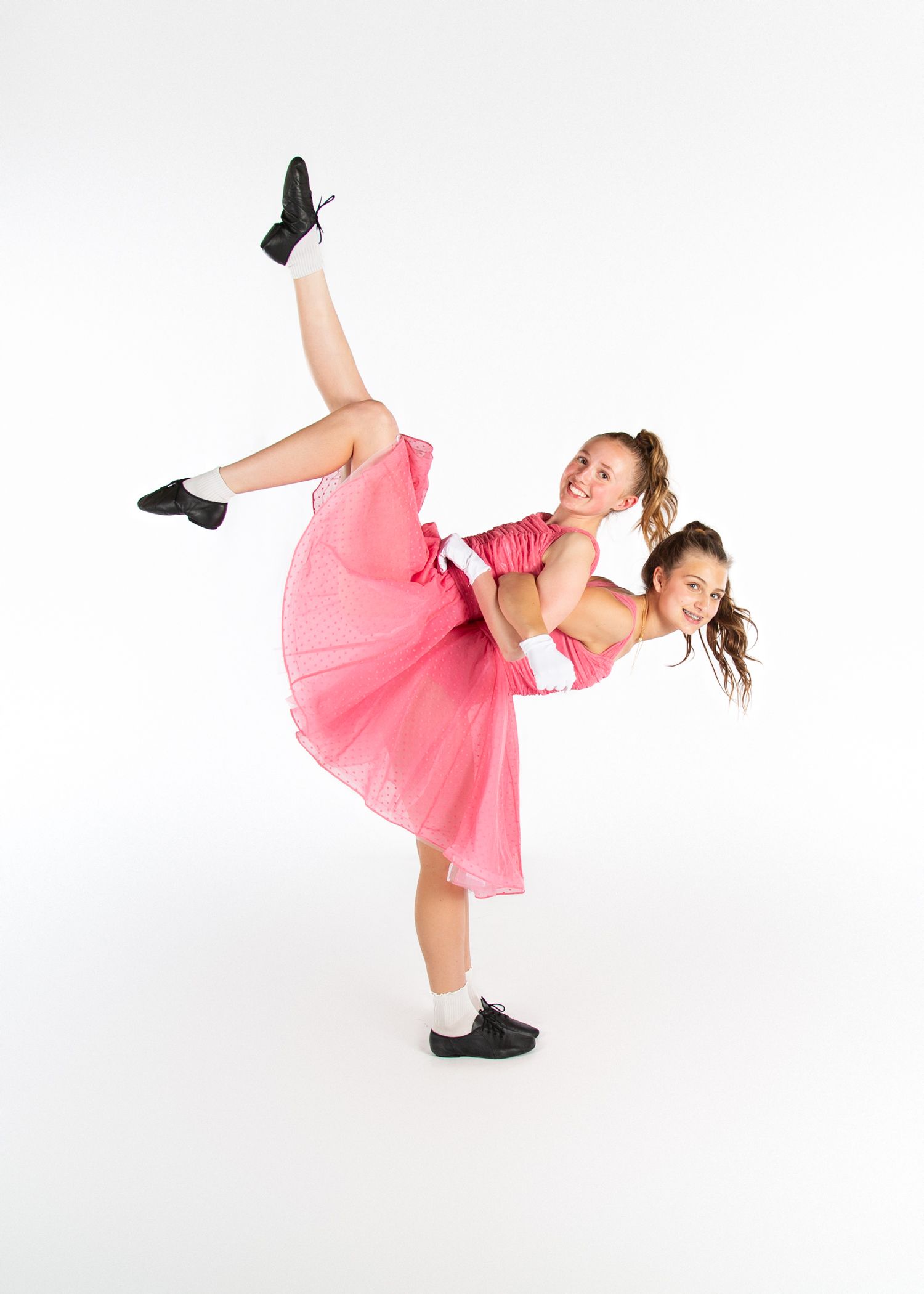 Two dancers in pink tutus strike a graceful pose together against a white backdrop.