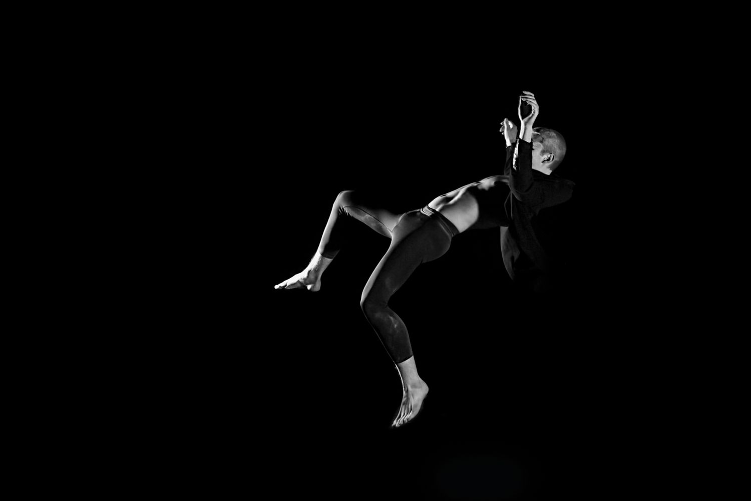 Dramatic black and white photograph of a dancer suspended in mid-air against a dark background.