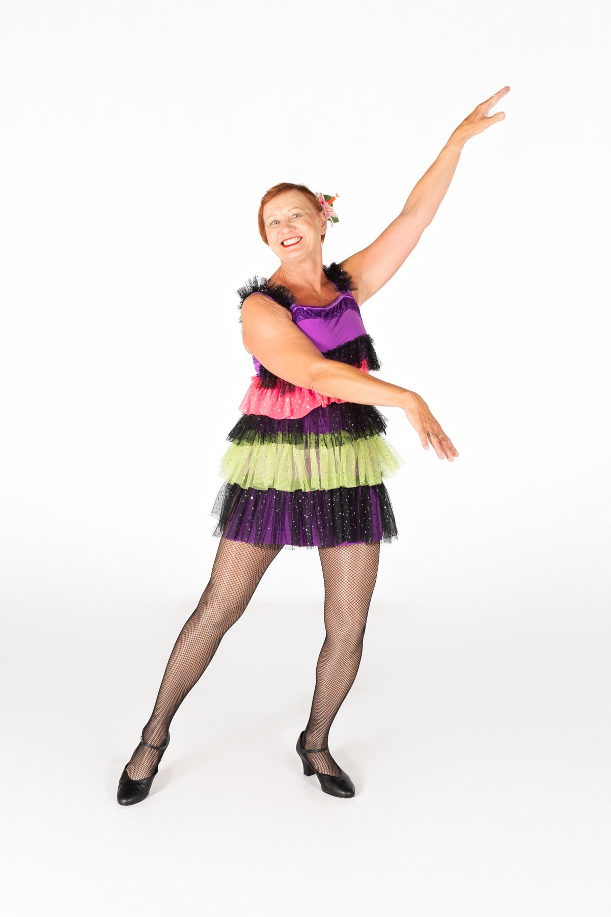 A dancer in a colorful tiered dress with black, pink, purple and green layers performs an energetic dance pose.