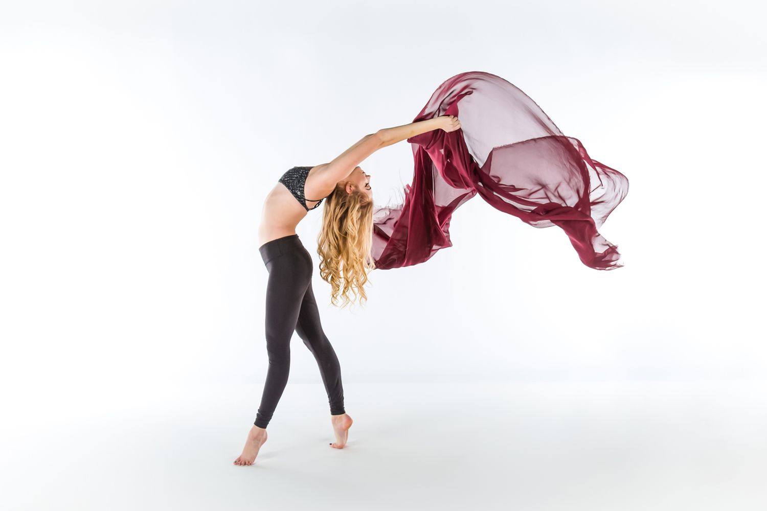 A dancer in black leggings performs with a flowing burgundy silk fabric against a white background.