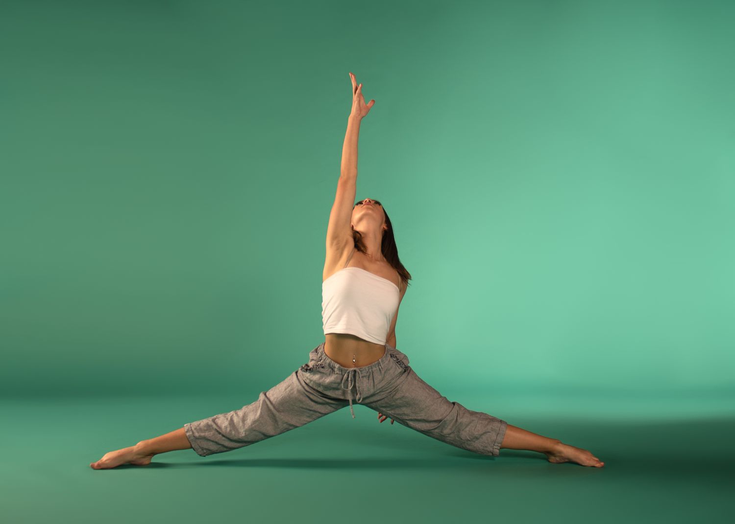 Athletic performer in stretchy cargo pants and crop top strikes a dramatic split pose against turquoise studio backdrop.