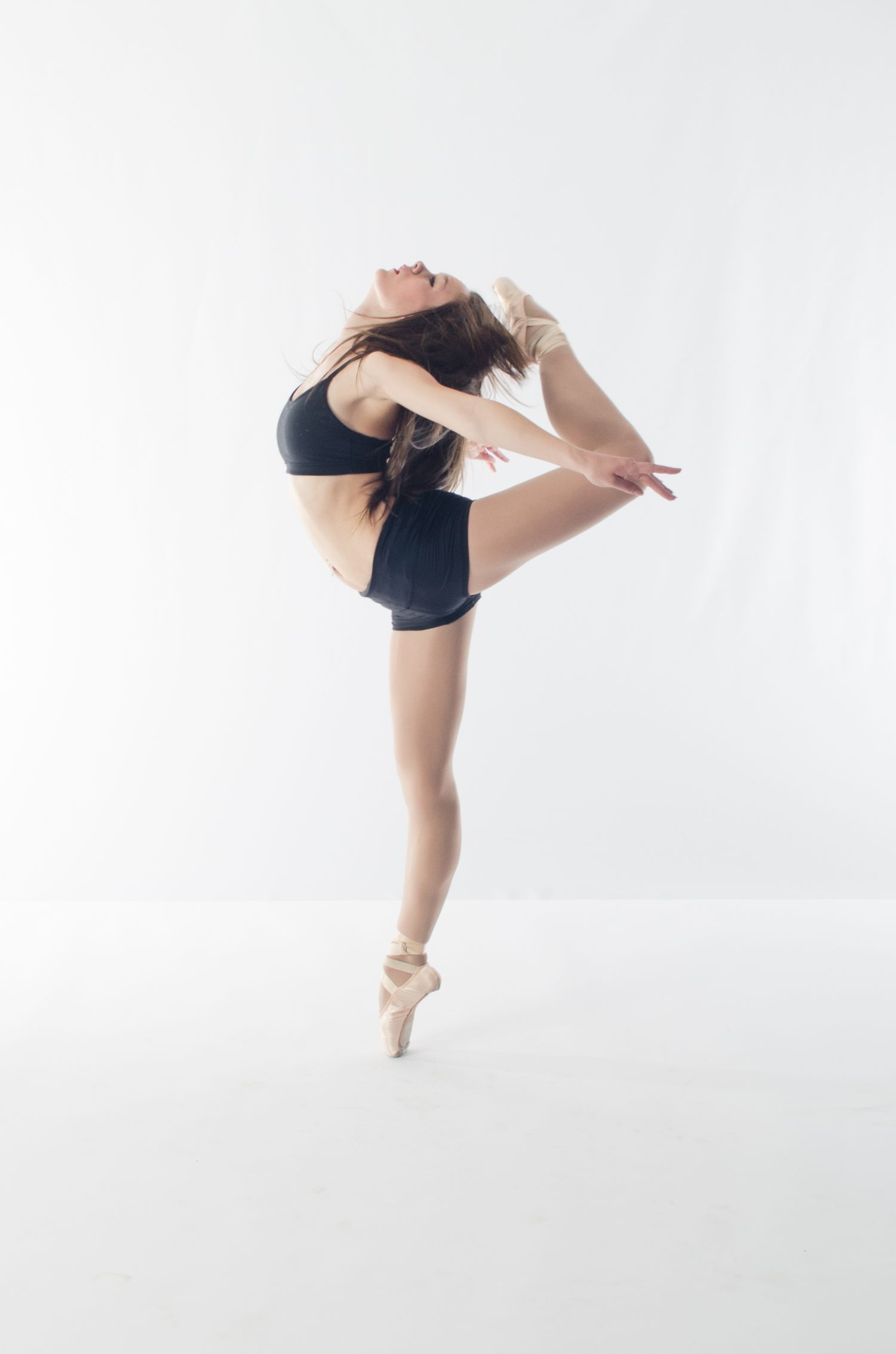 Ballet dancer executing elegant pose en pointe against white background.