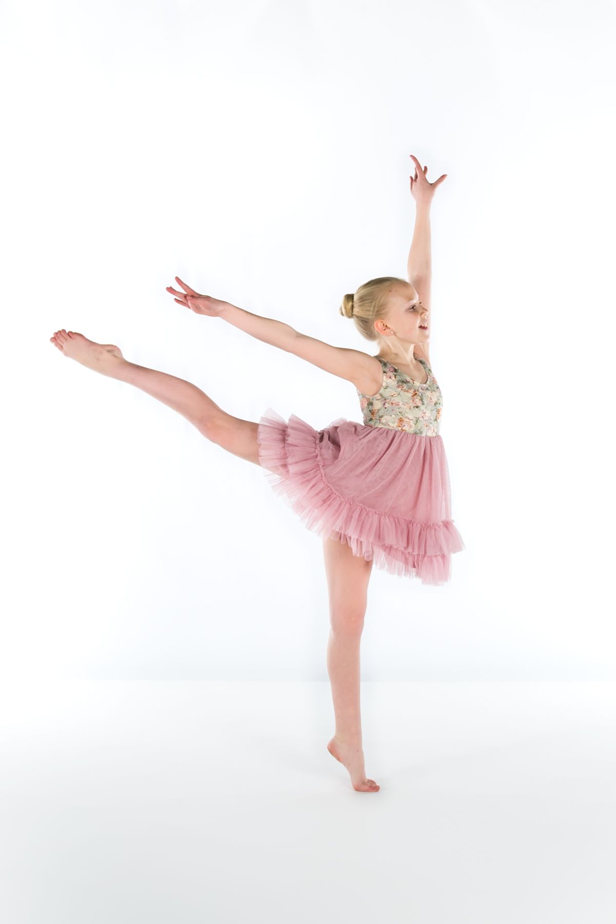 Young dancer in pink tutu performs graceful arabesque pose against white background.