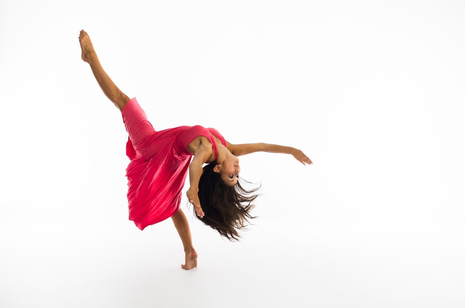 Contemporary dancer in red dress performs expressive movement against white backdrop.