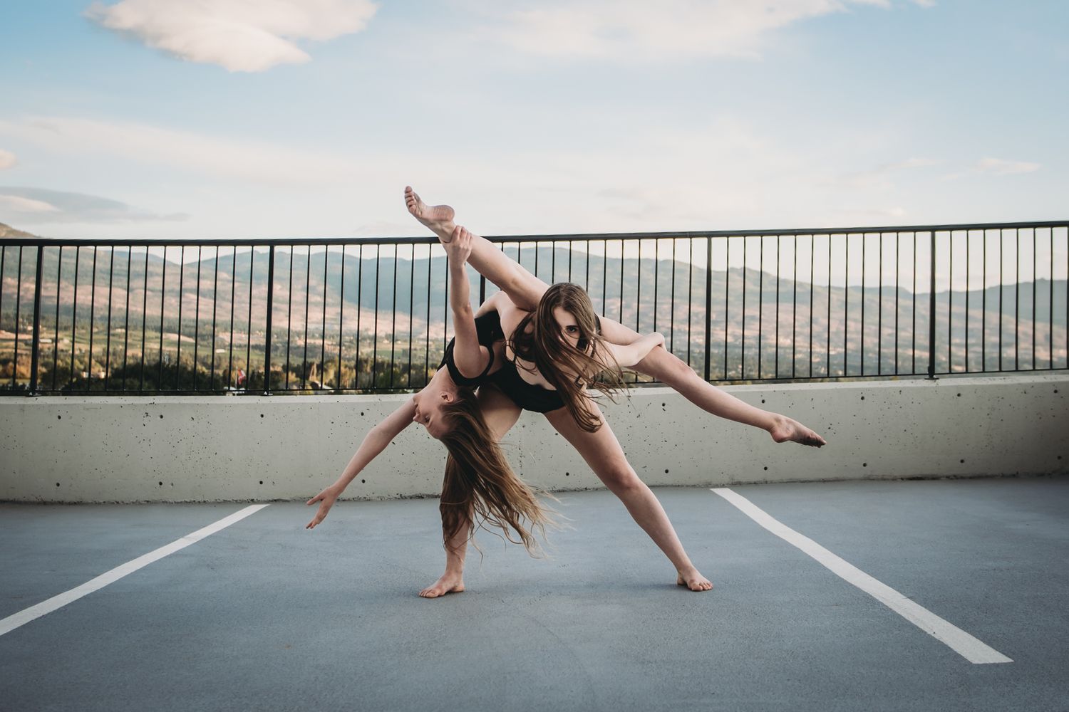Dancers performing a graceful contemporary duet on an urban rooftop with cityscape views in the background.