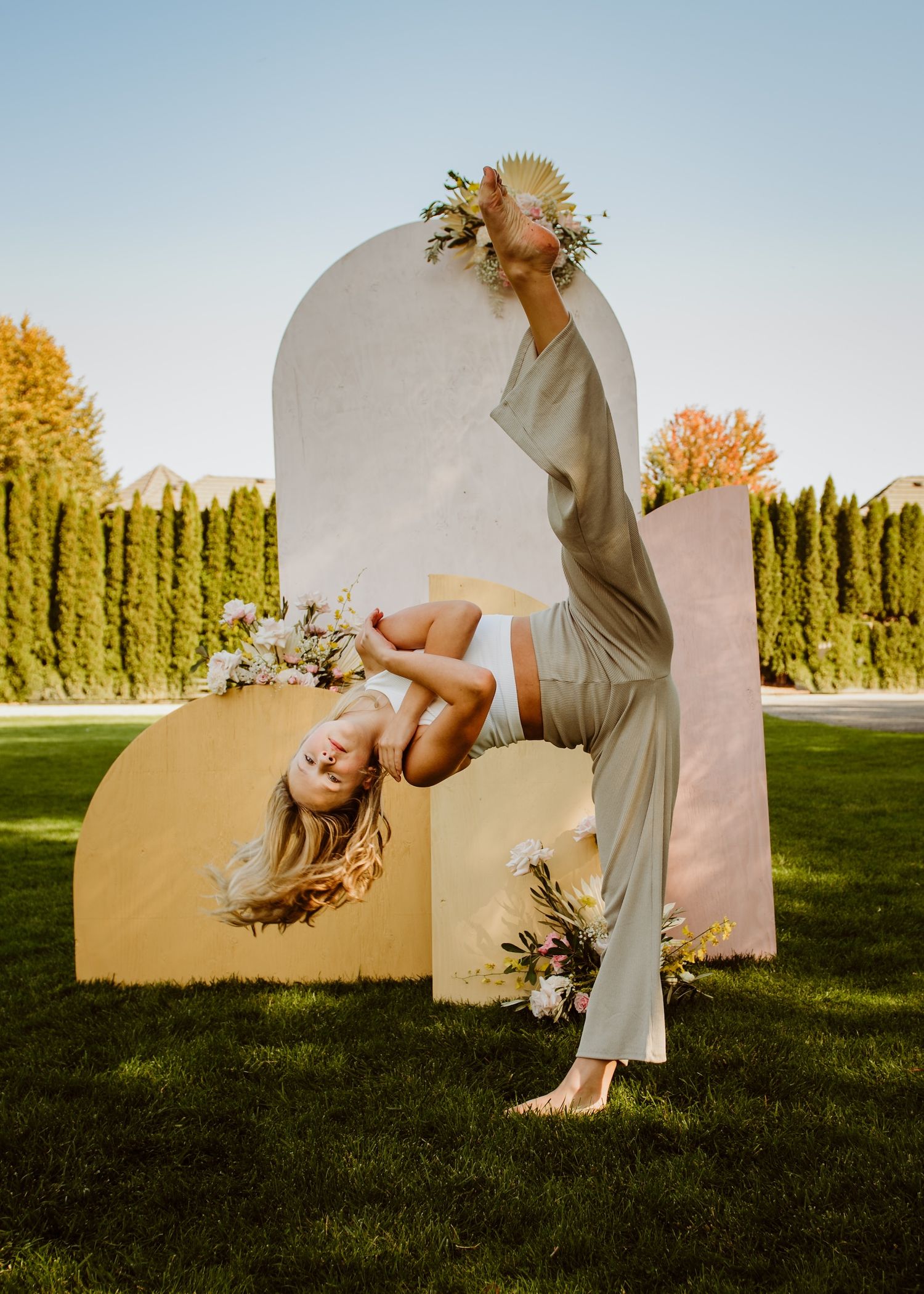 Artistic outdoor pose with curved architectural elements and floral accents in warm sunlight.