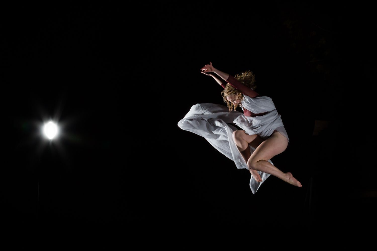 A dancer in white leaps gracefully through the air against a dark night sky with a glowing moon in the background.