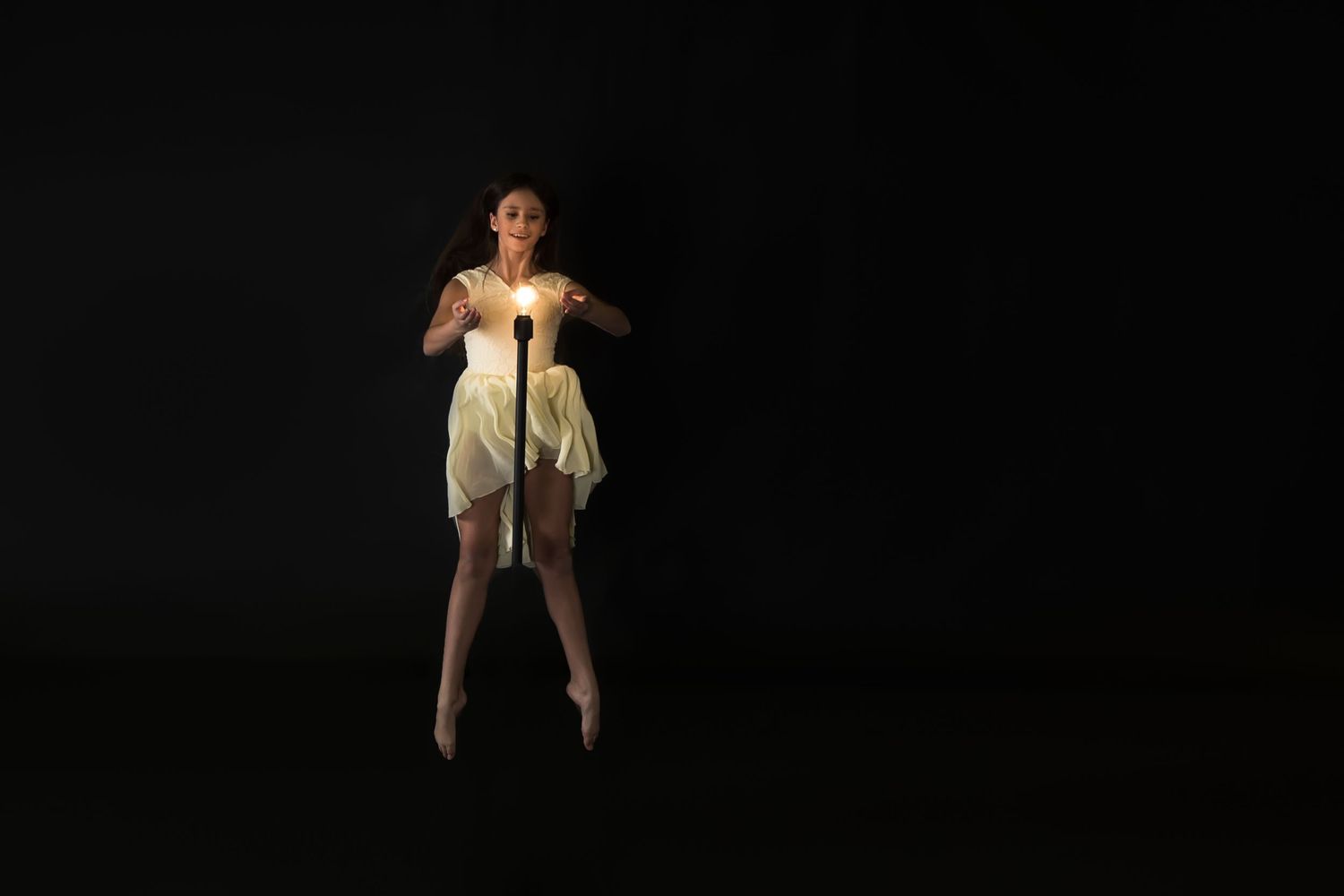 A performer in a white dress stands in a dramatic spotlight against a dark background.