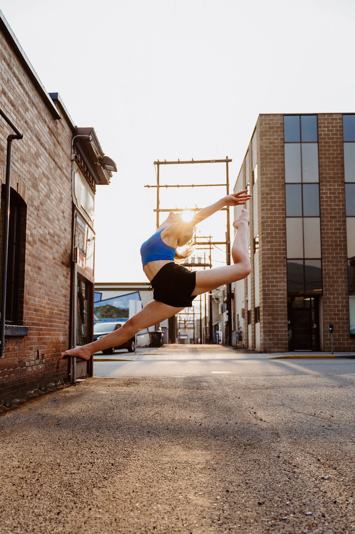A dancer performs a graceful leap in an urban alleyway between brick buildings during golden hour.