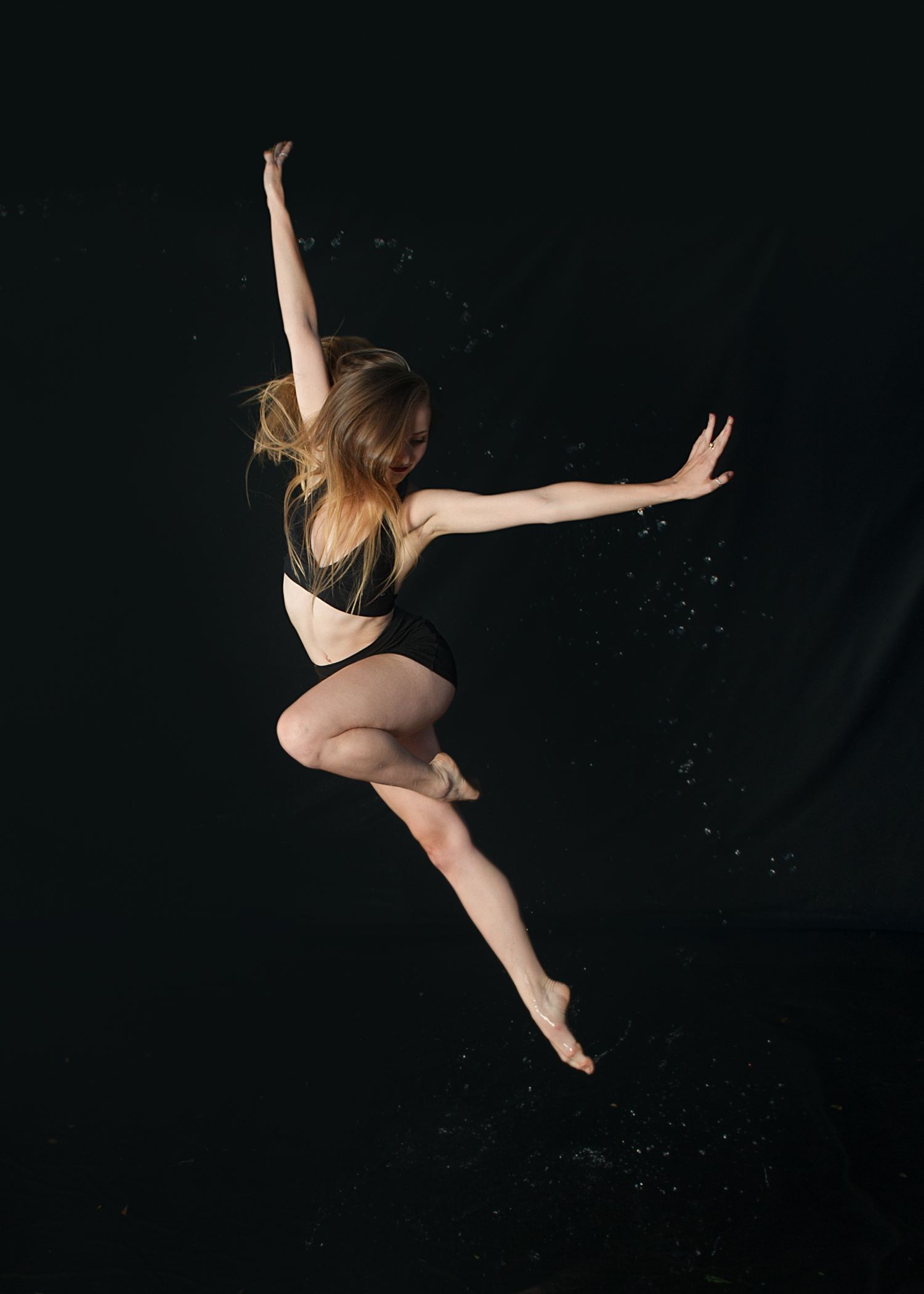 A dancer leaps gracefully against a dark background with arms outstretched in a dynamic dance pose.