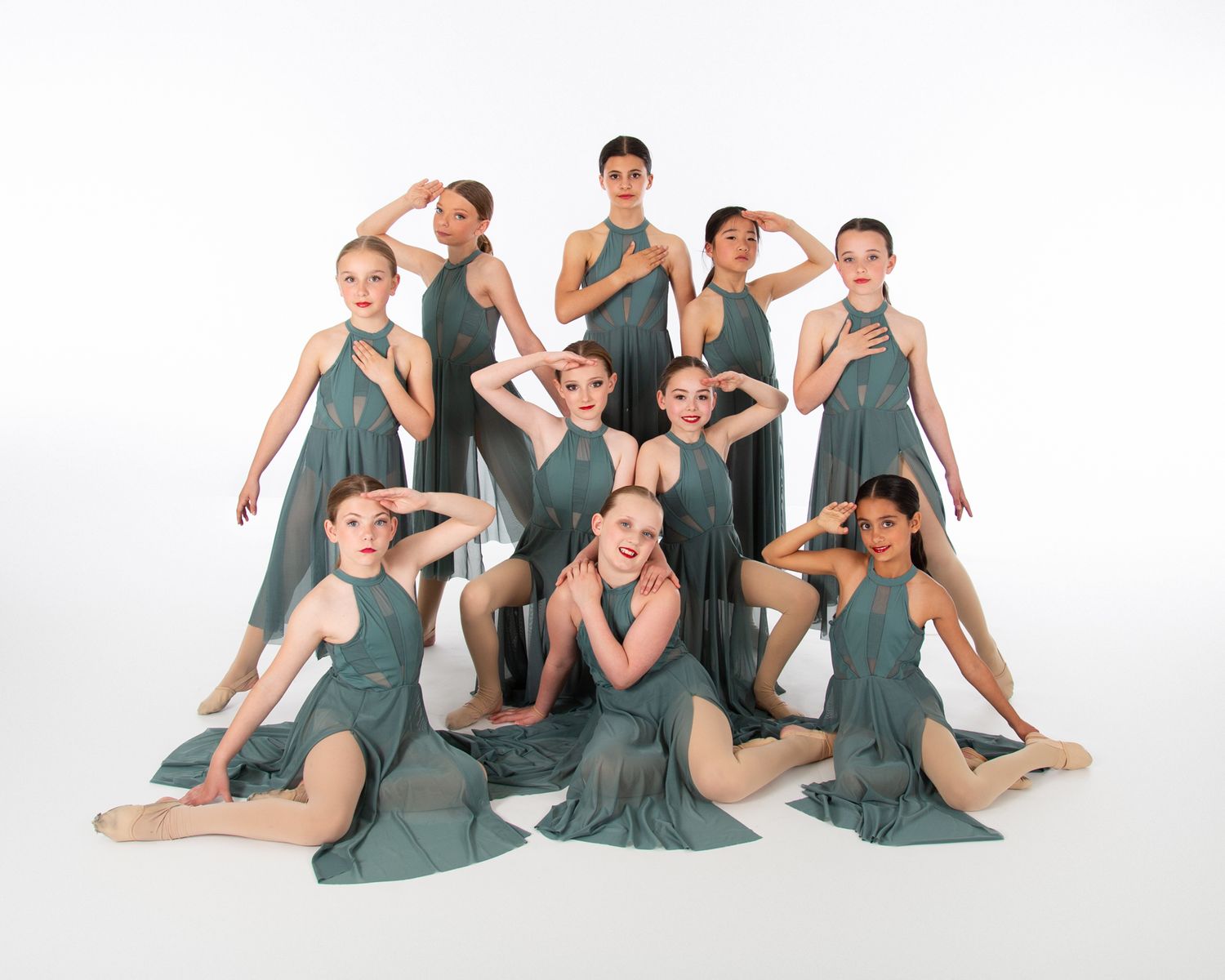 Dancers in flowing sage green dresses pose gracefully together in artistic formation against white background.