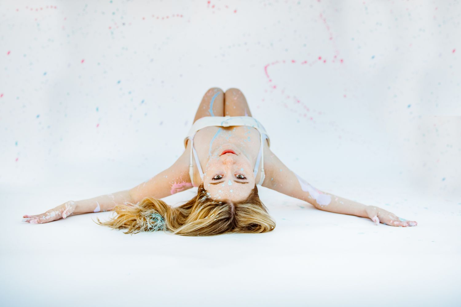 A person wearing virtual reality goggles lies on their back with arms spread out against a white background.