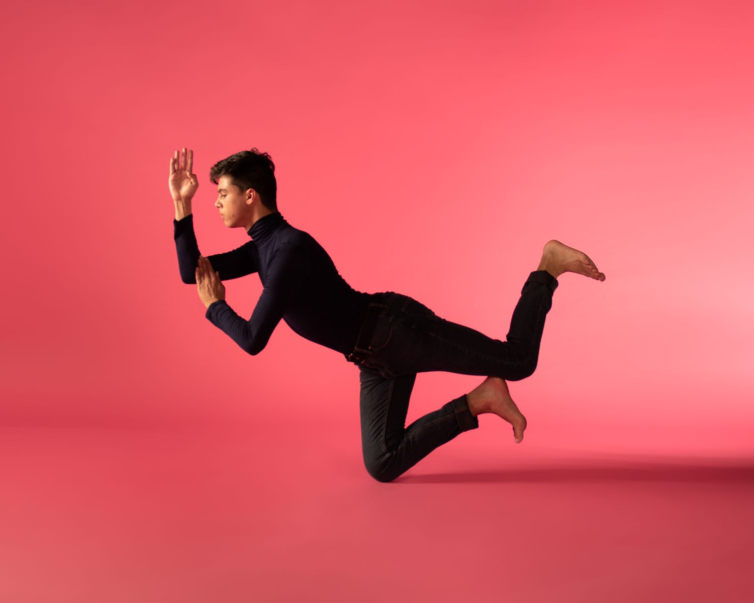 Person in black outfit appears to be floating horizontally against a vibrant pink background in a studio setting.
